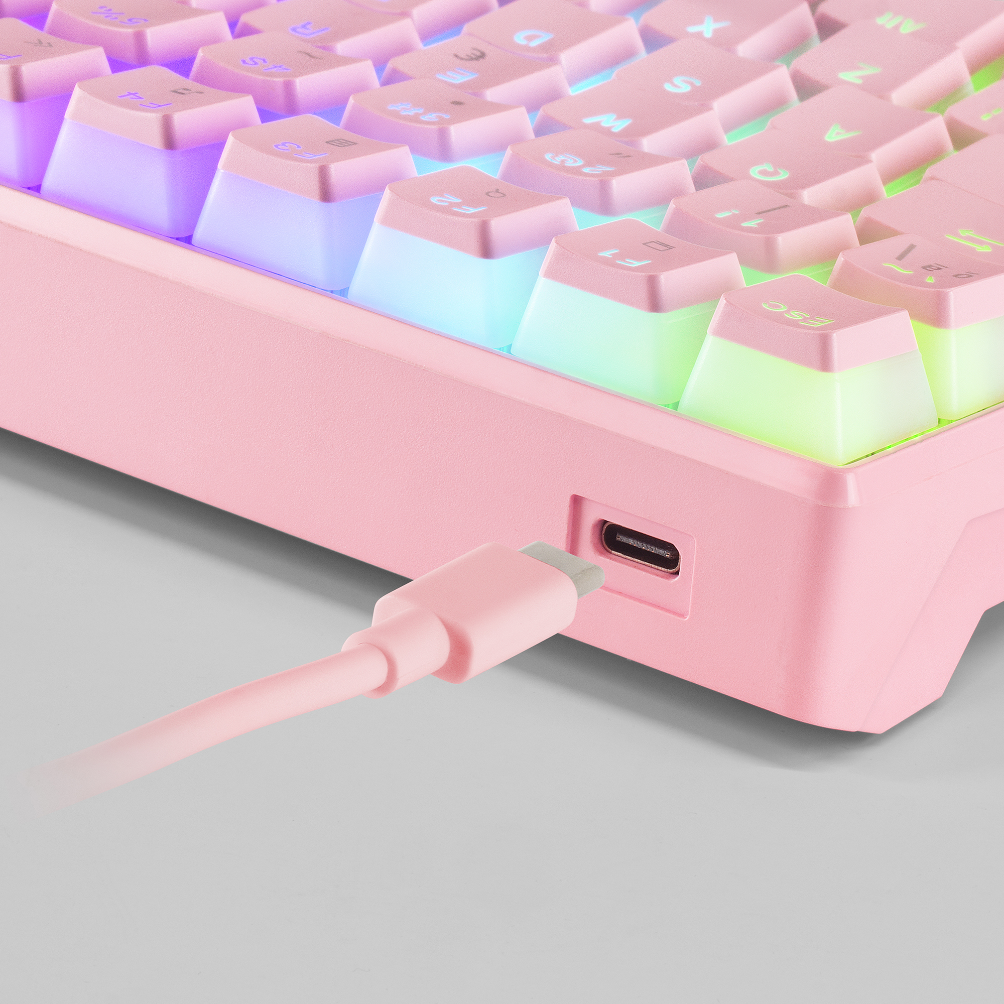 Primer plano de un teclado rosa con un cable de carga enchufado. Las teclas están retroiluminadas.