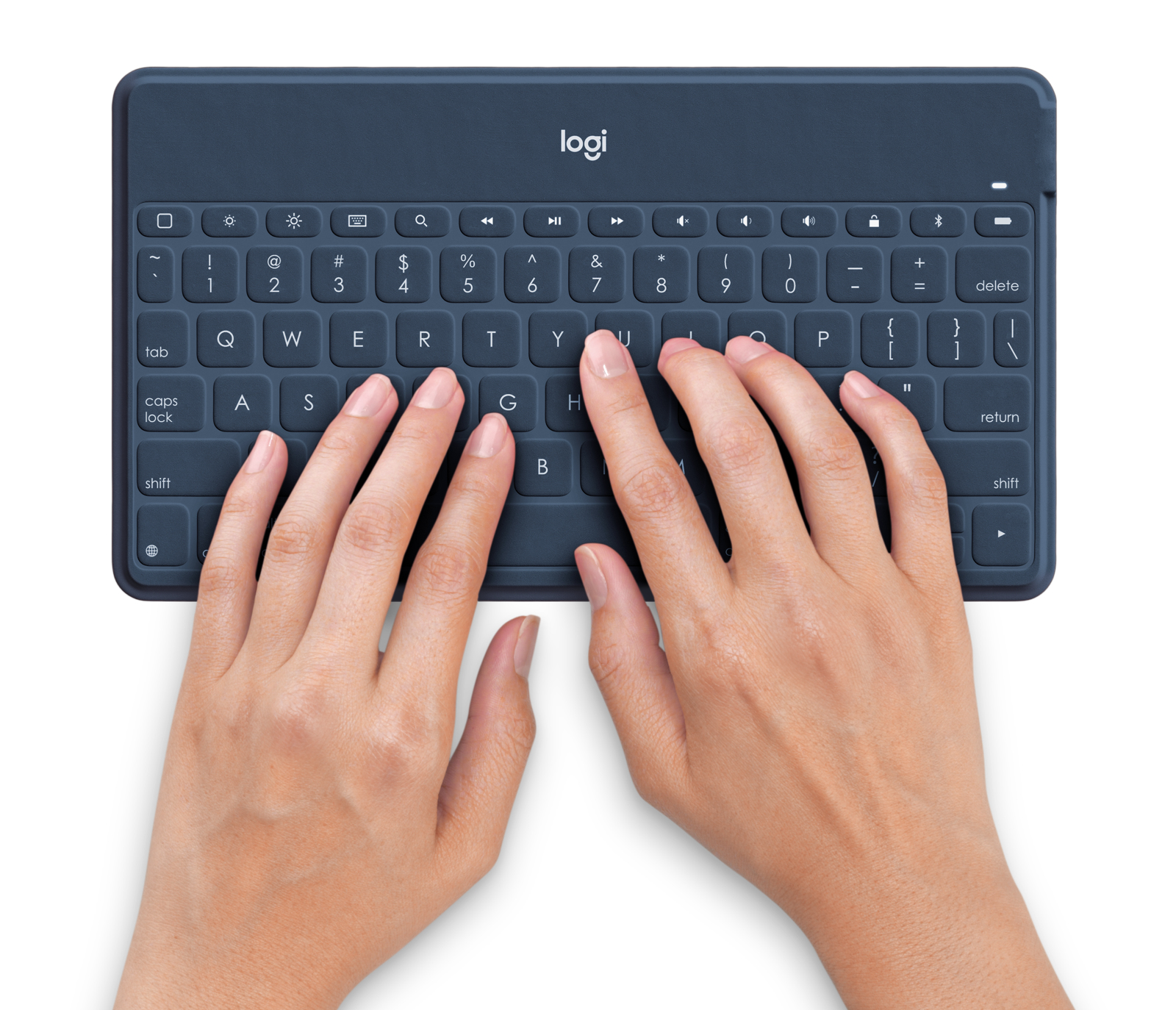 Mani che digitano su una tastiera blu navy con etichette bianche, su una superficie bianca.