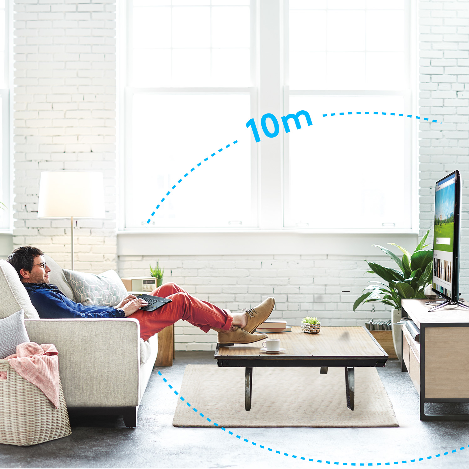 Mężczyzna siedzi na kanapie, używając laptopa i oglądając telewizję w salonie.