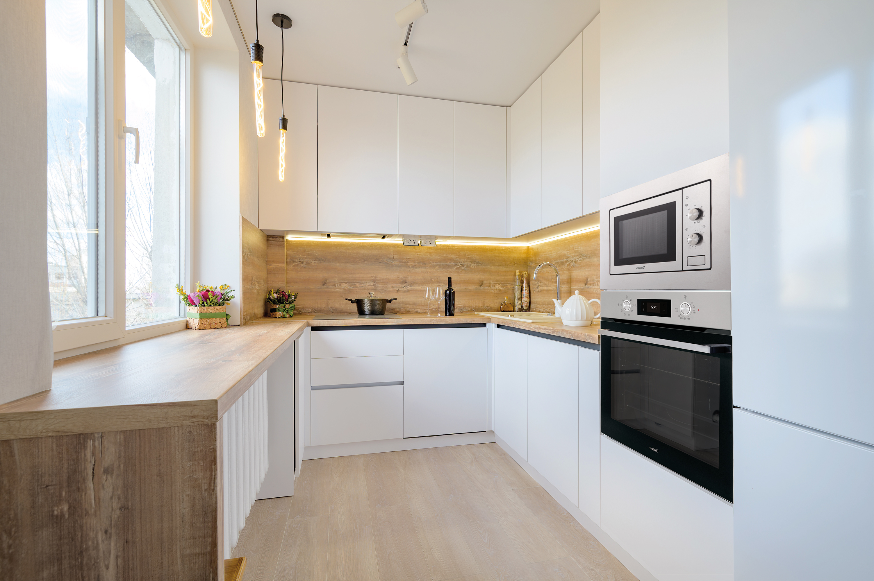 Nowoczesne wnętrze kuchni z białymi szafkami, drewnianym blatem i urządzeniami.