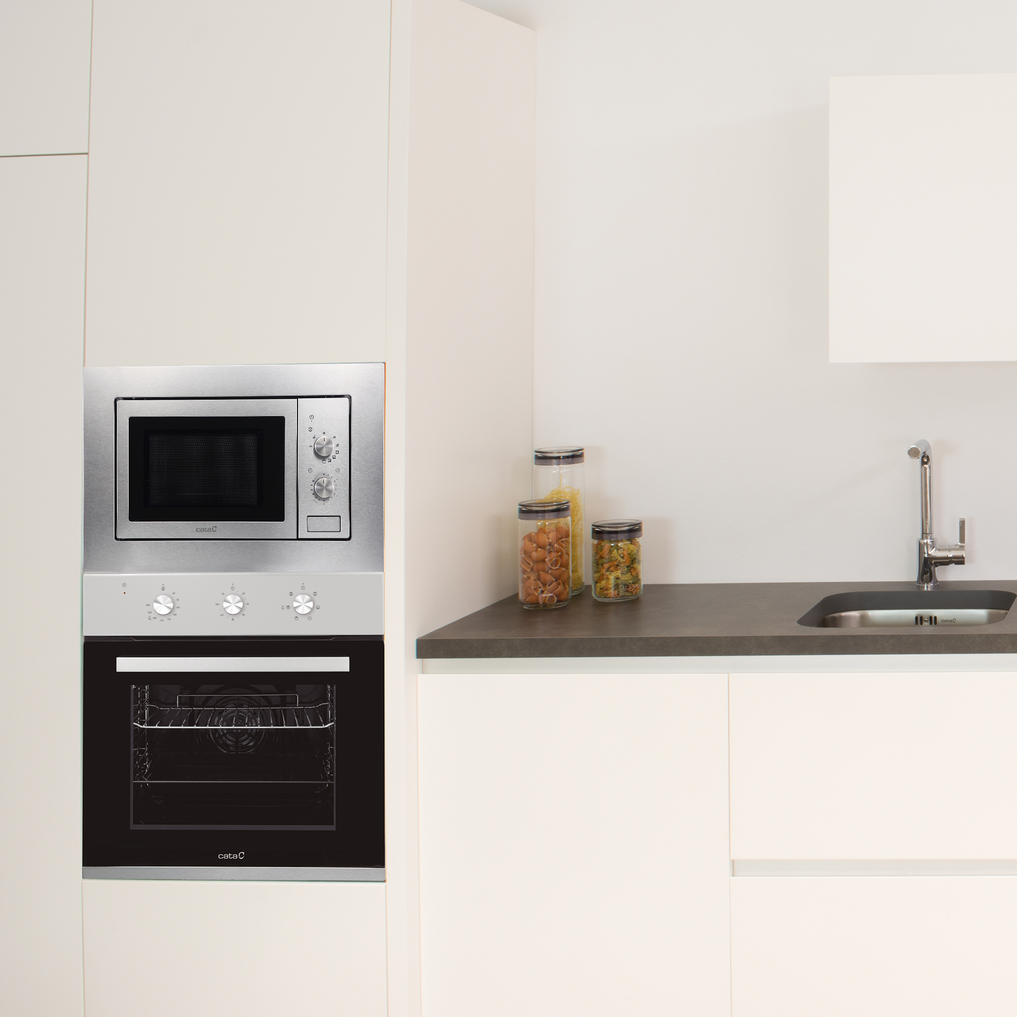 Wnętrze kuchni z wbudowaną kuchenką mikrofalową i piekarnikiem, blatem, słoikami i zlewem.