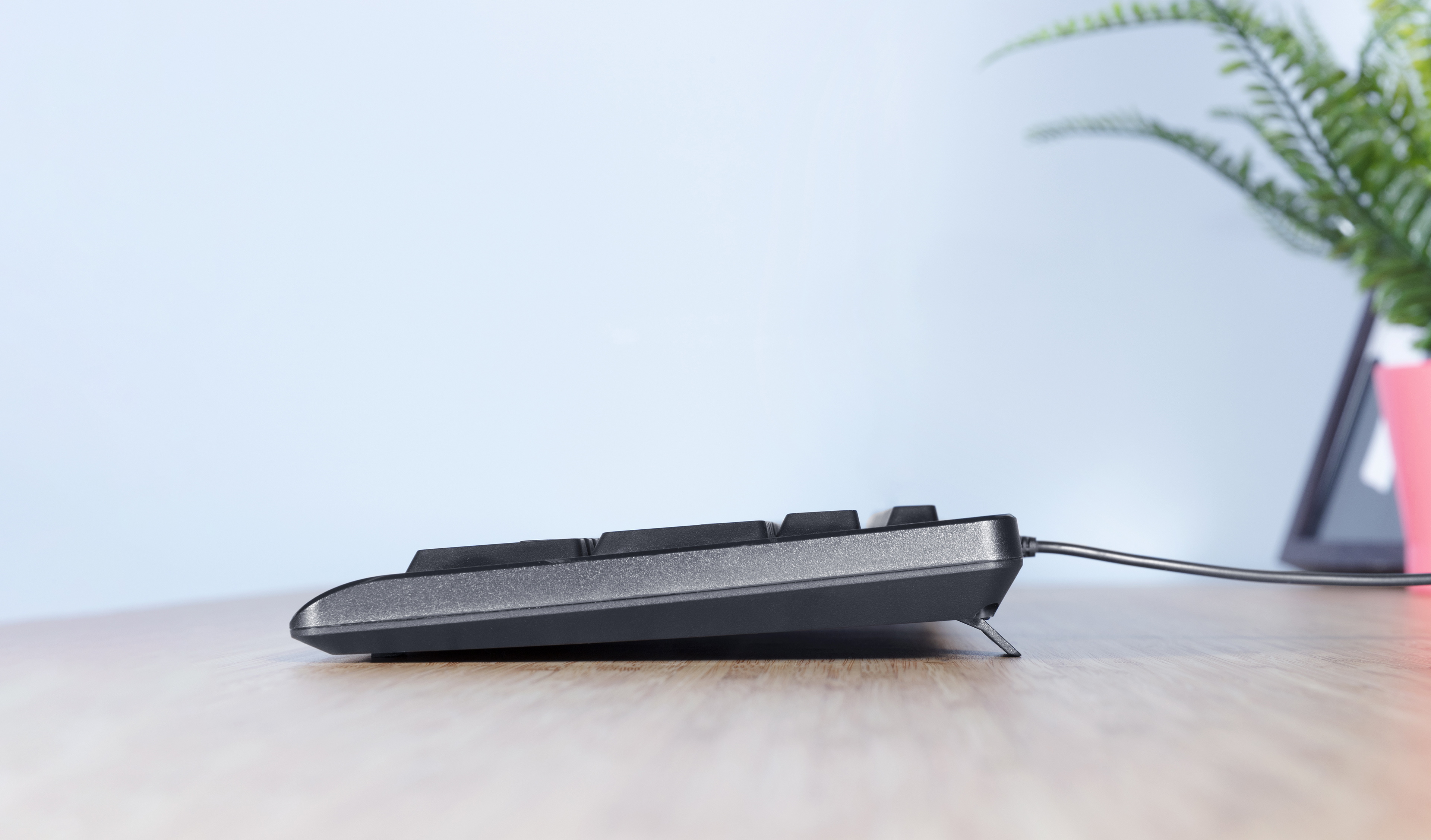 Widok z boku czarnej klawiatury z kablem na drewnianym biurku.