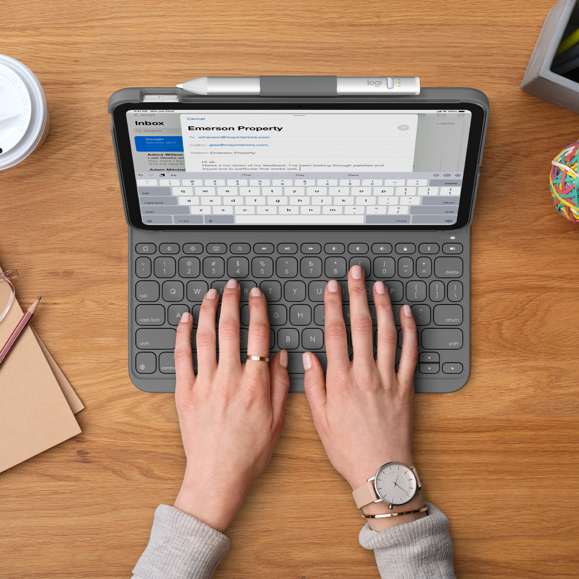 Hände tippen auf Tablet-Tastatur mit Stift, Uhr und Kaffeetasse auf Holzschreibtisch.