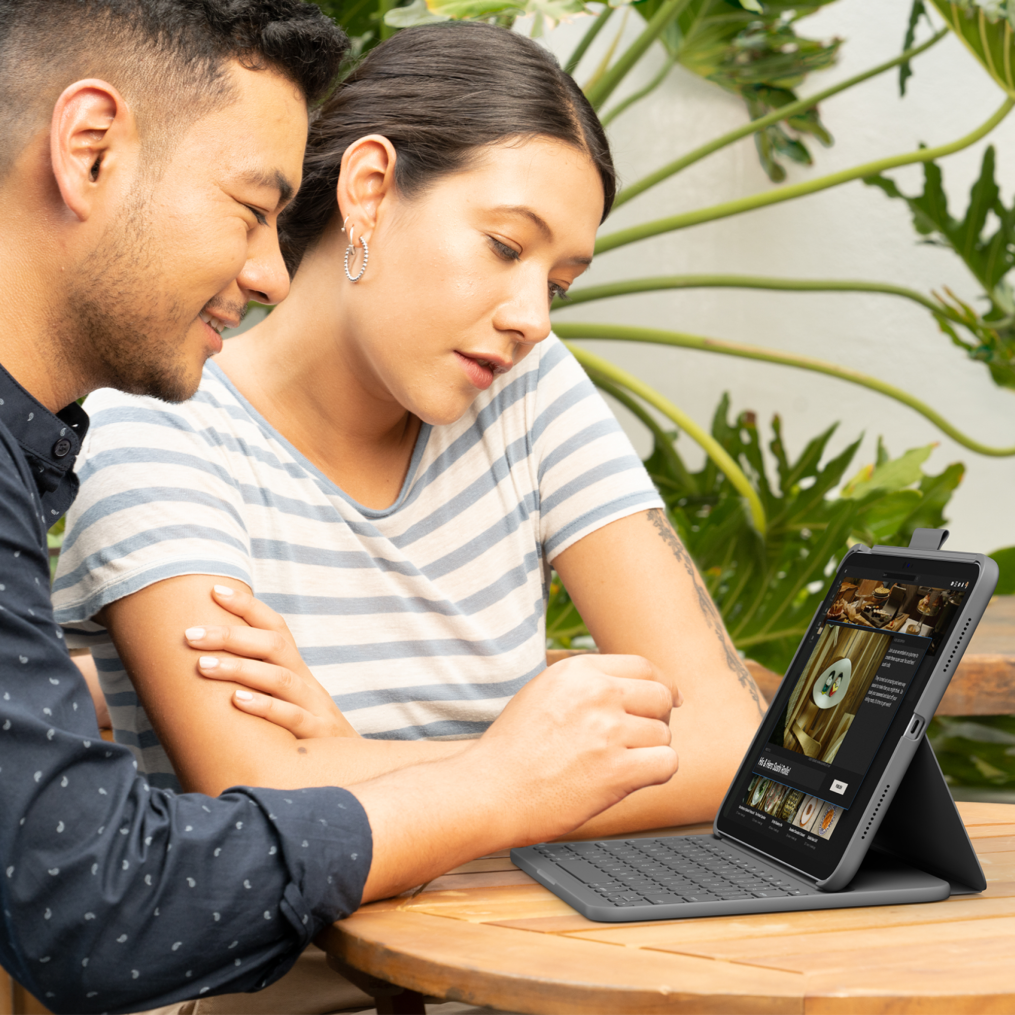 Zwei Personen betrachten ein Tablet mit angeschlossener Tastatur im Freien mit grünem Laub.
