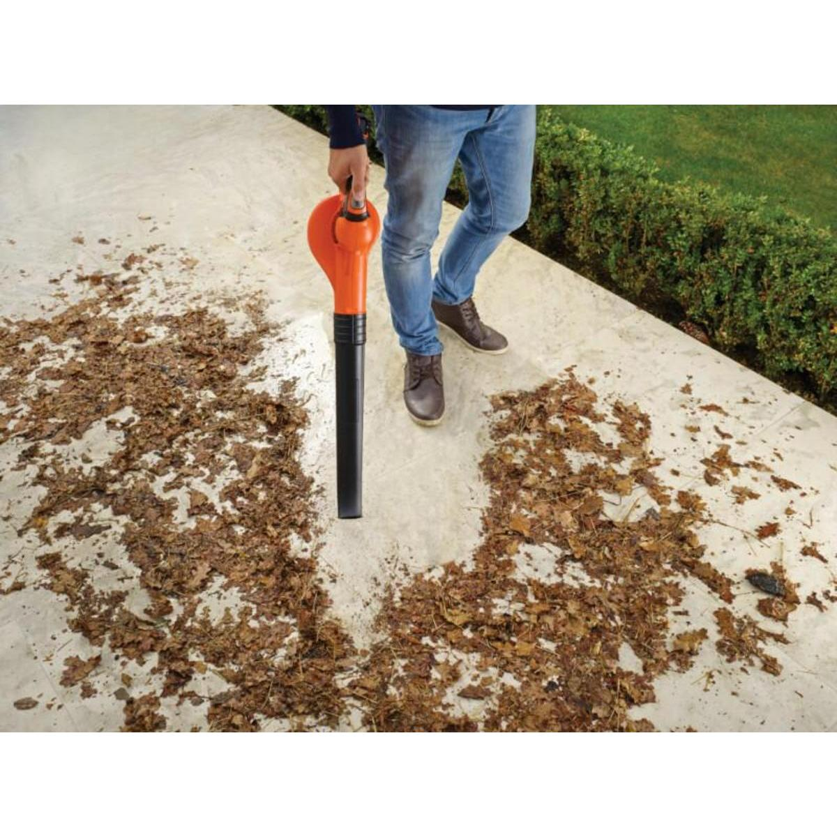 Een persoon die een bladblazer gebruikt op een betonnen oppervlak bedekt met gevallen bladeren.