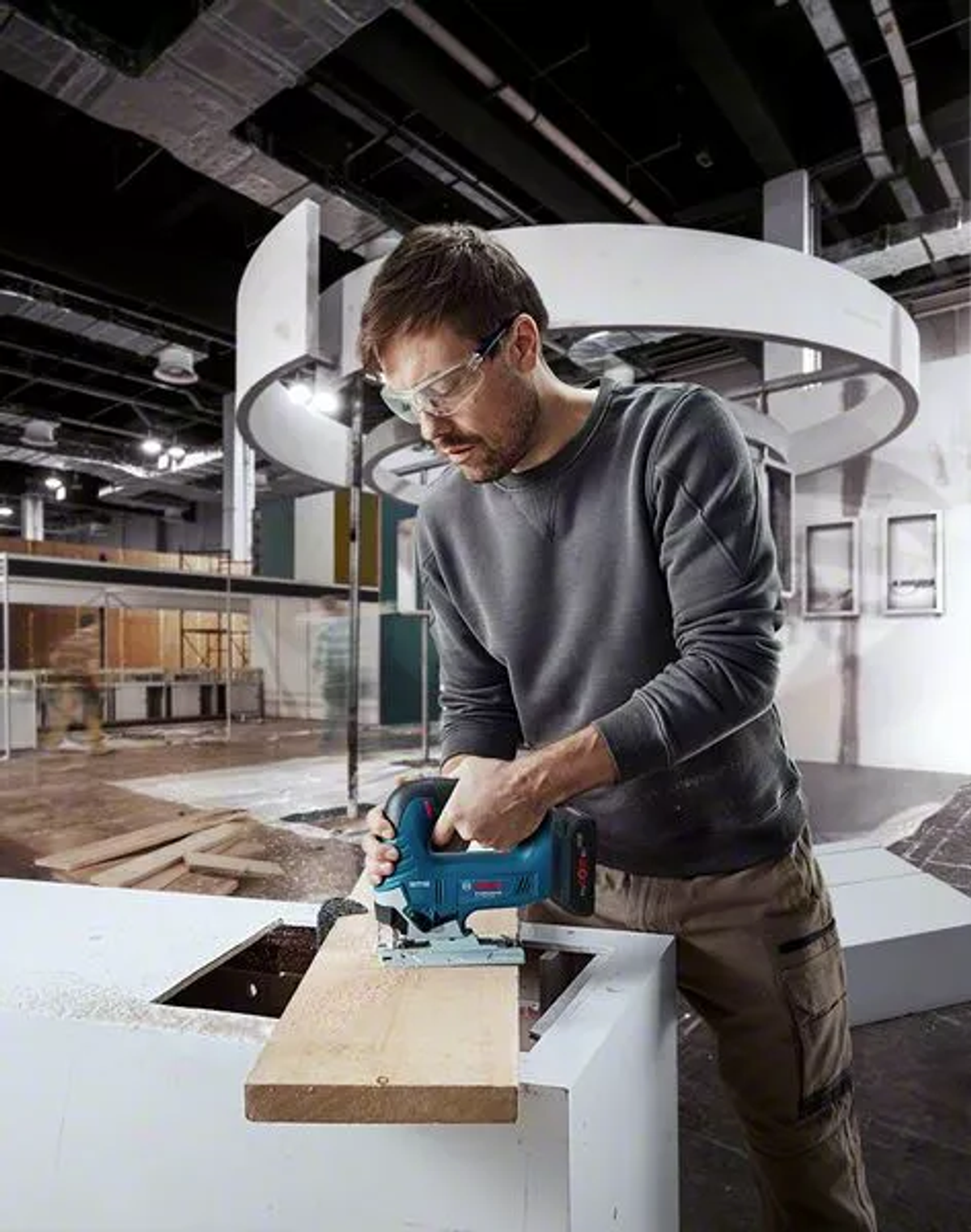 Uomo che usa un seghetto alternativo su una tavola di legno. Indossa occhiali protettivi, in un'officina.