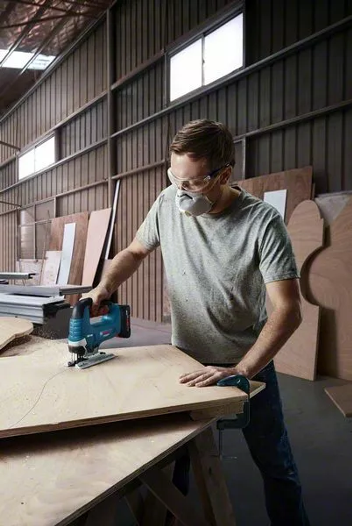 Un uomo in un'officina sta tagliando una tavola di legno con un seghetto alternativo blu.