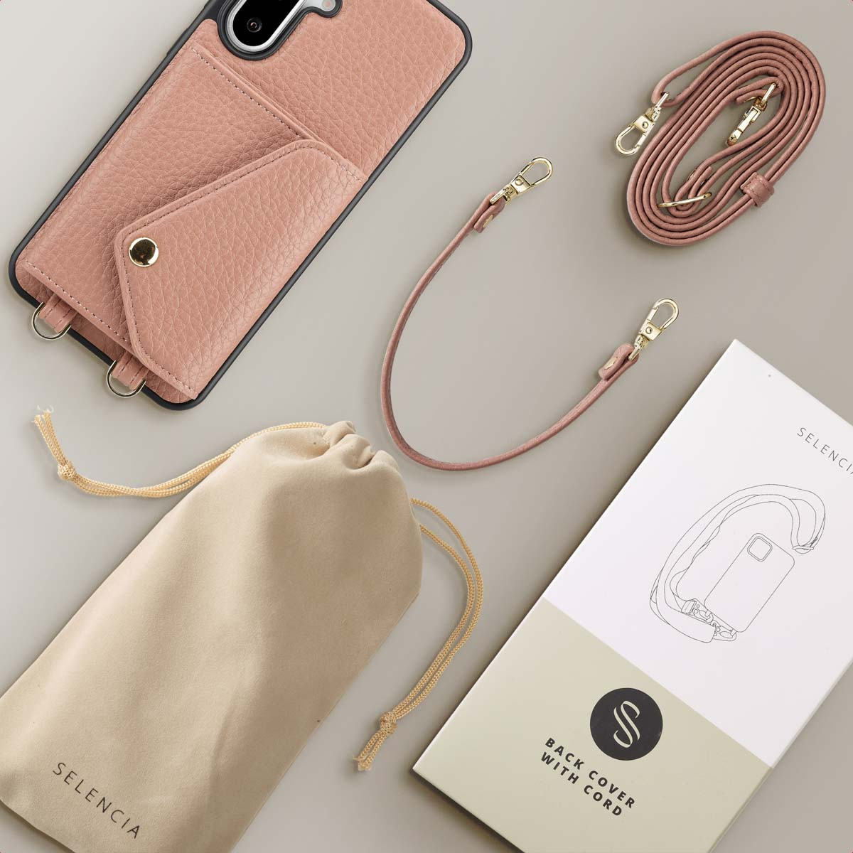 Roze telefoonhoesje met koord, zakje en doos op een grijze ondergrond.