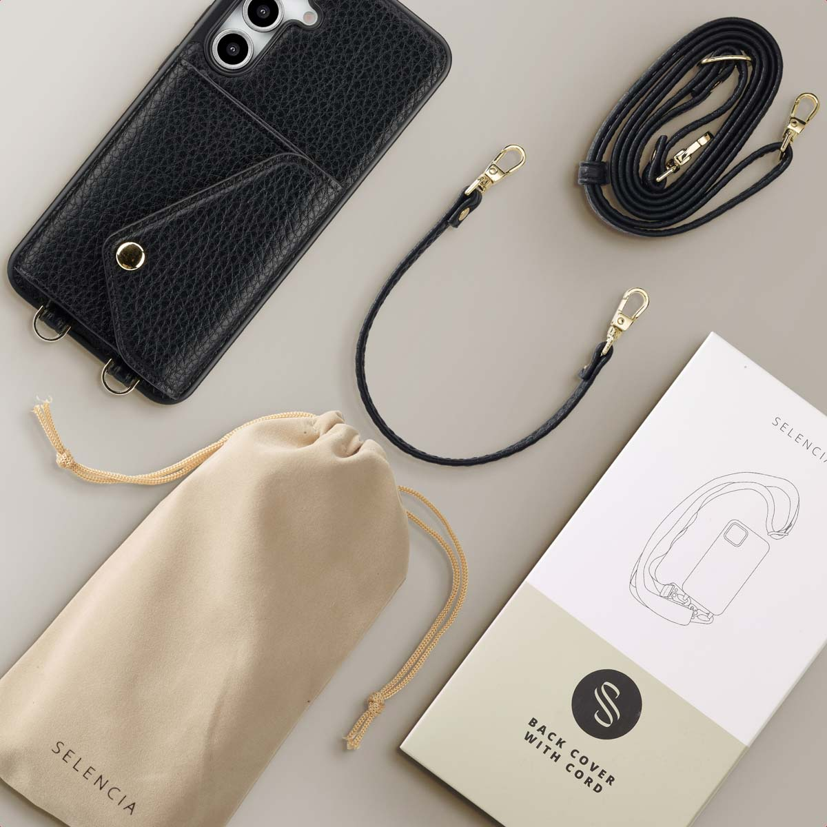 Custodia nera con cinturino. Custodia, cinturino e confezione su superficie grigia. Borsa beige presente.