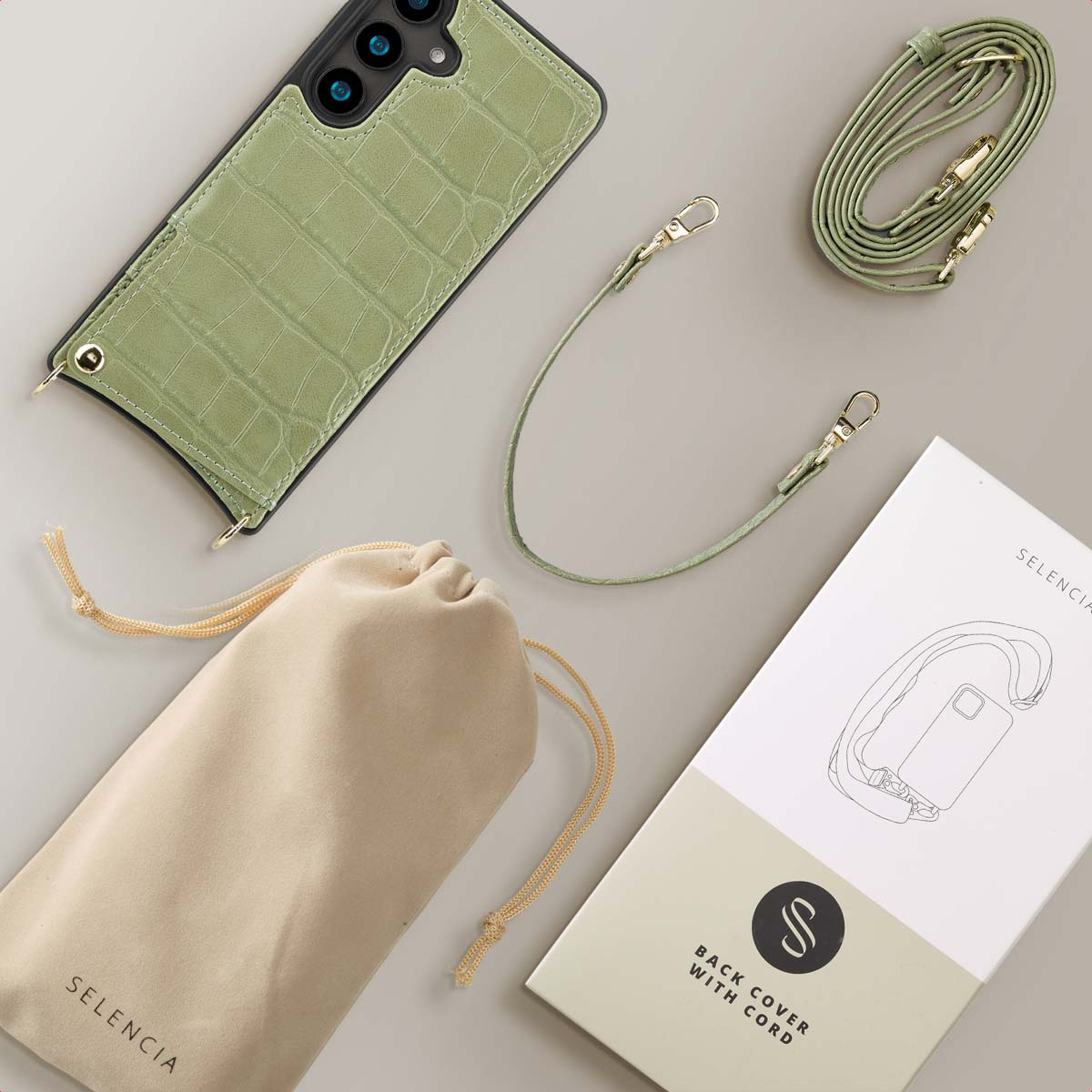 Groene telefoonhoes met riem, zakje en doos. Alles gerangschikt op een grijs oppervlak.