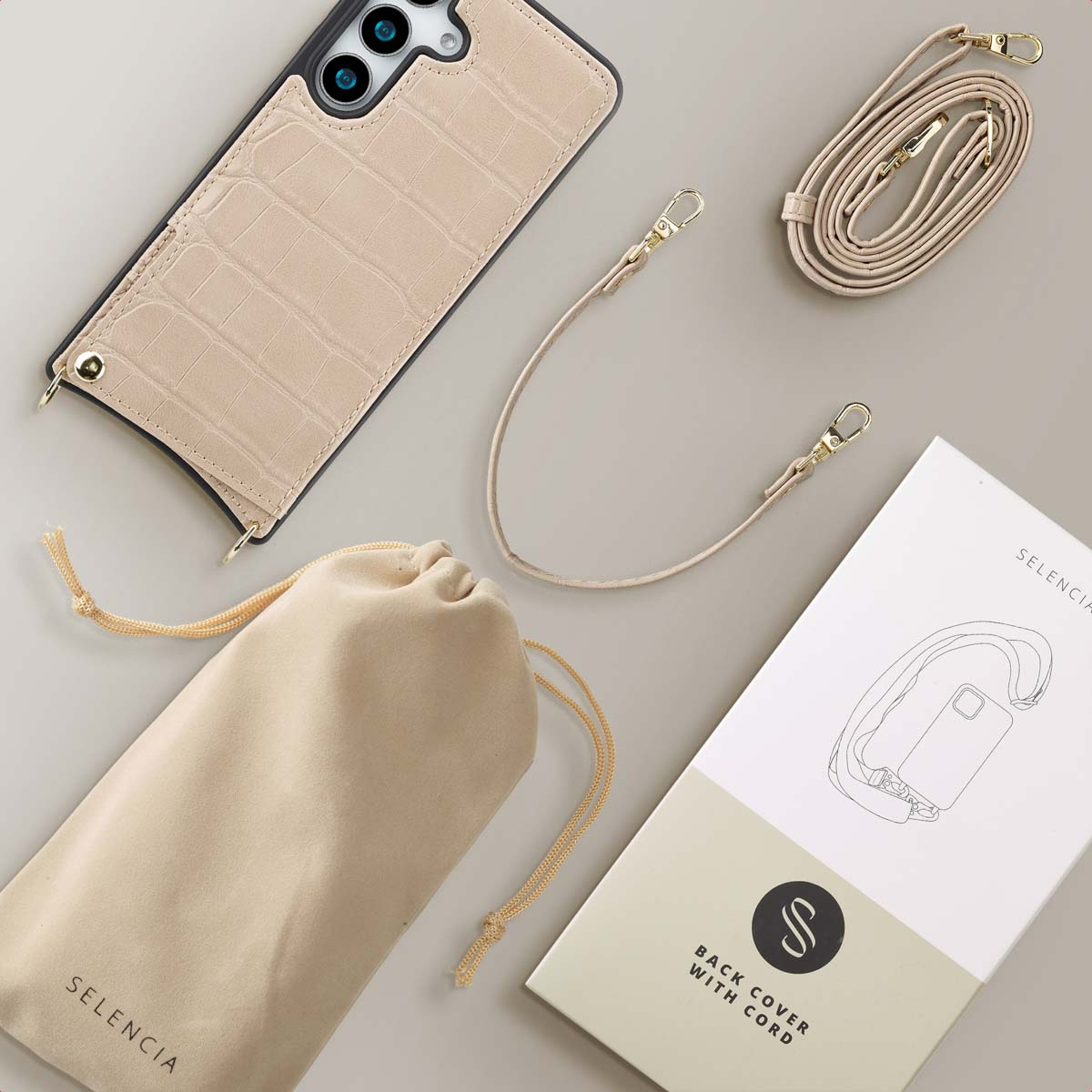 Beige leren telefoonhoes met riem, een tas en een doos op een tafel.