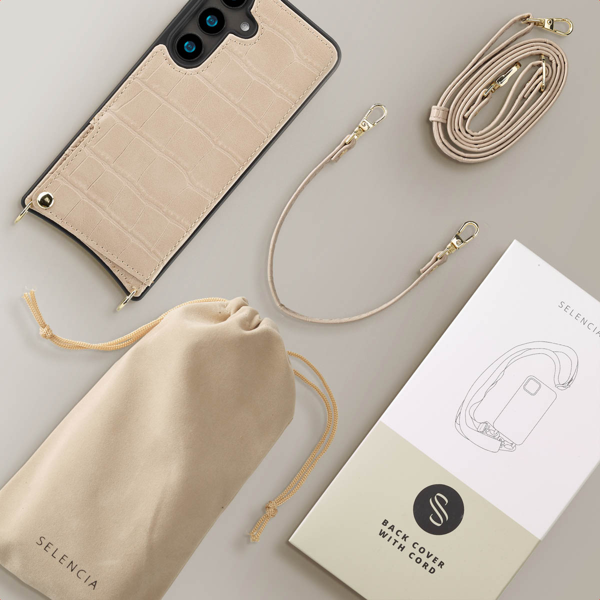 Beige telefoonhoesje met riem, zakje en doos op grijze ondergrond. Op de doos staat 'SELENCIA'. Croco-achtige textuur.