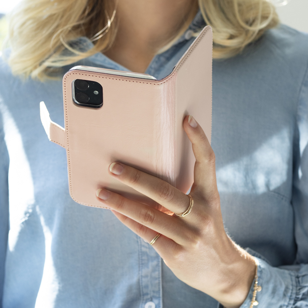 Een vrouw die een roze telefoonhoes vasthoudt, met een telefoon erin, handen, nagels en sieraden zichtbaar.