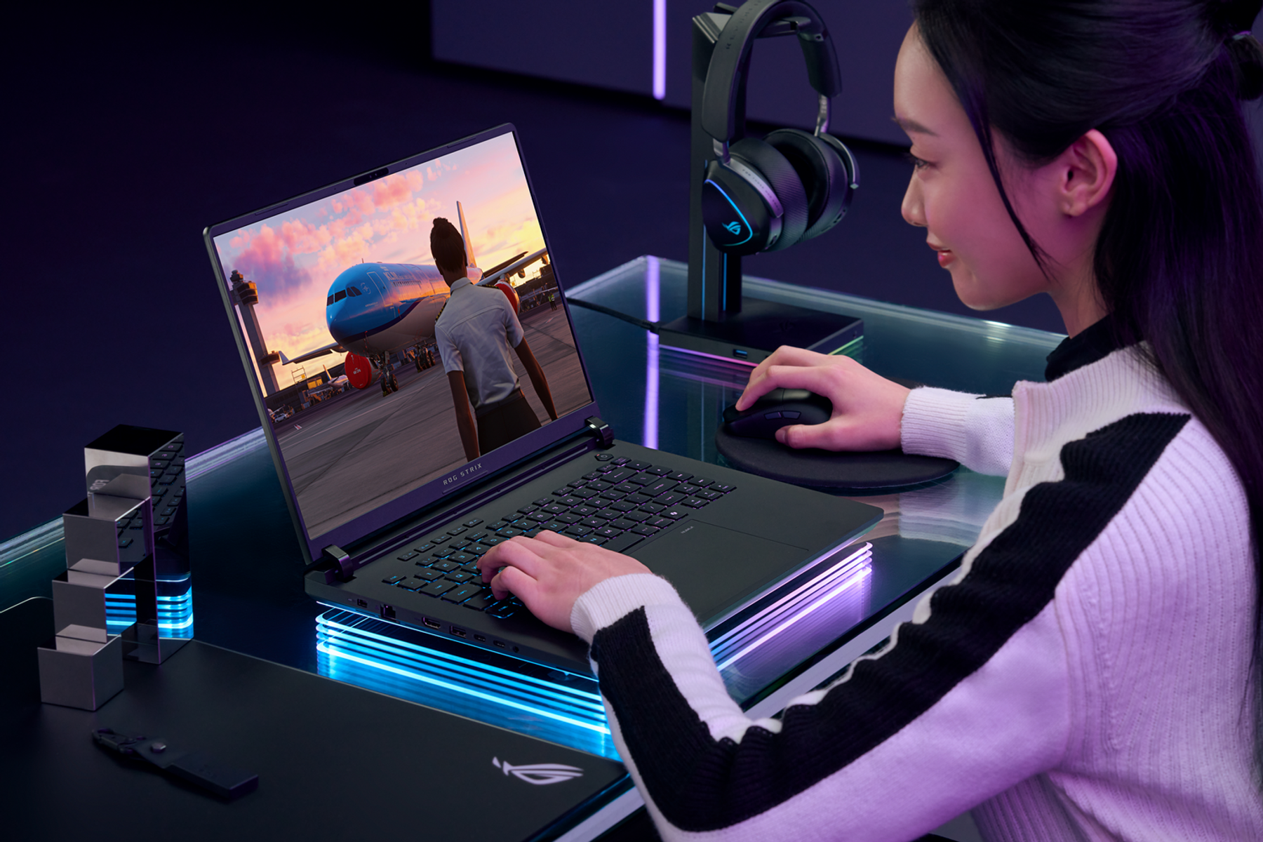 Kobieta korzystająca z laptopa. Ekran laptopa pokazuje samolot. Słuchawki po prawej. Mysz na biurku.