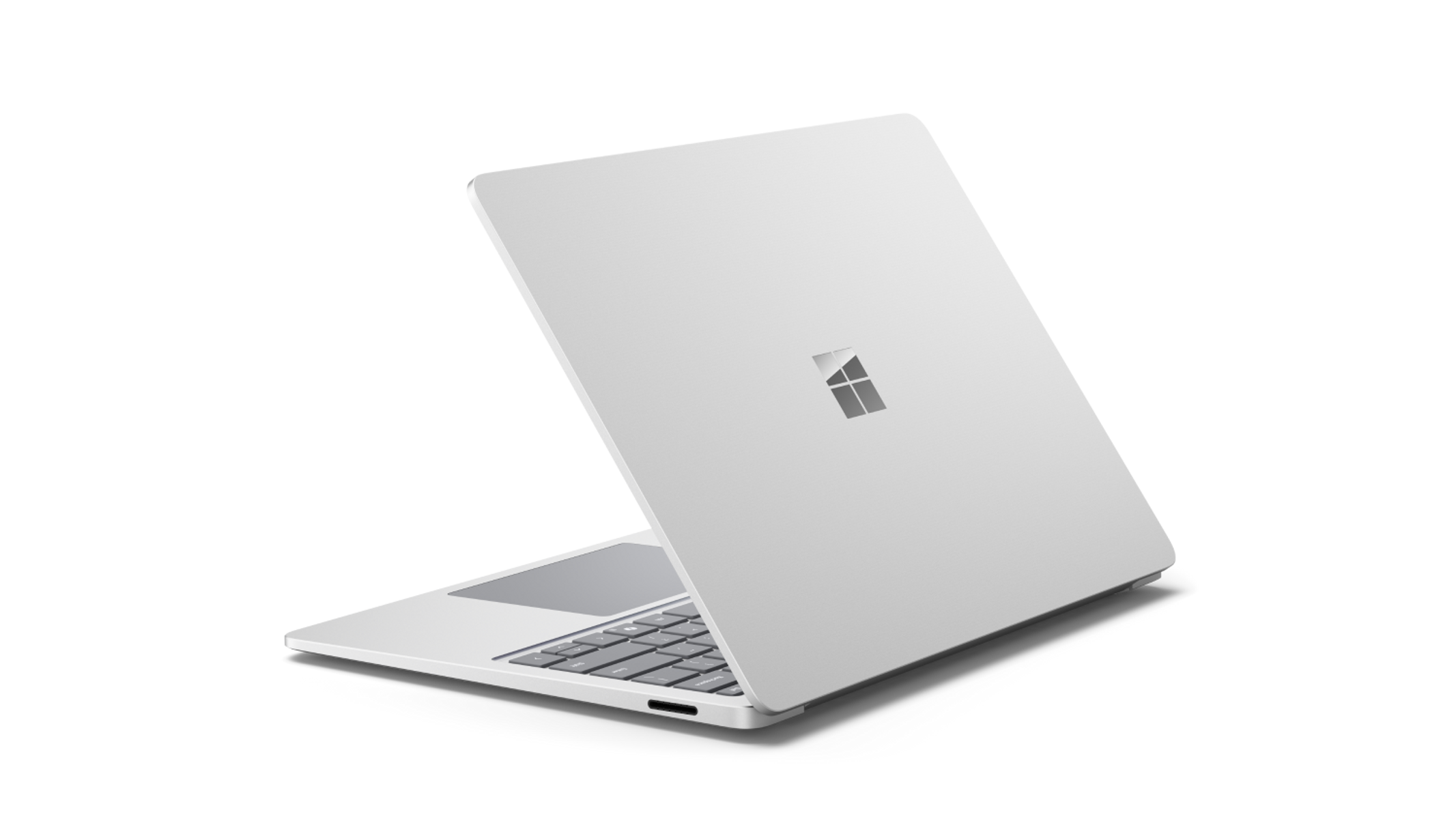 Portátil plateado, ligeramente abierto, con el logo de Microsoft en la parte trasera, sobre fondo negro.
