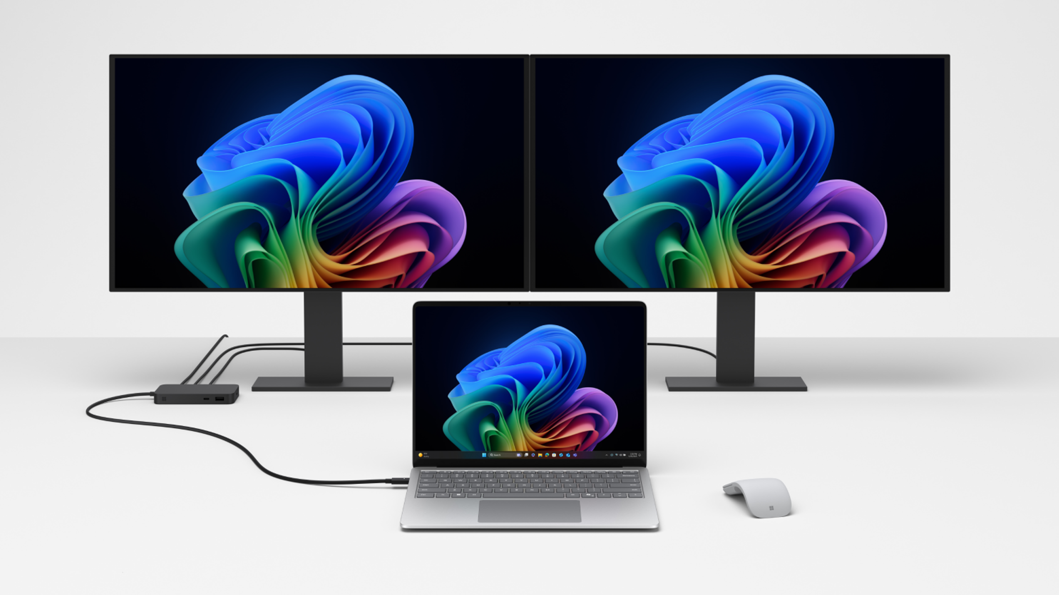 Dos monitores mostrando imágenes coloridas conectados a un portátil. Un ratón blanco está en la mesa.