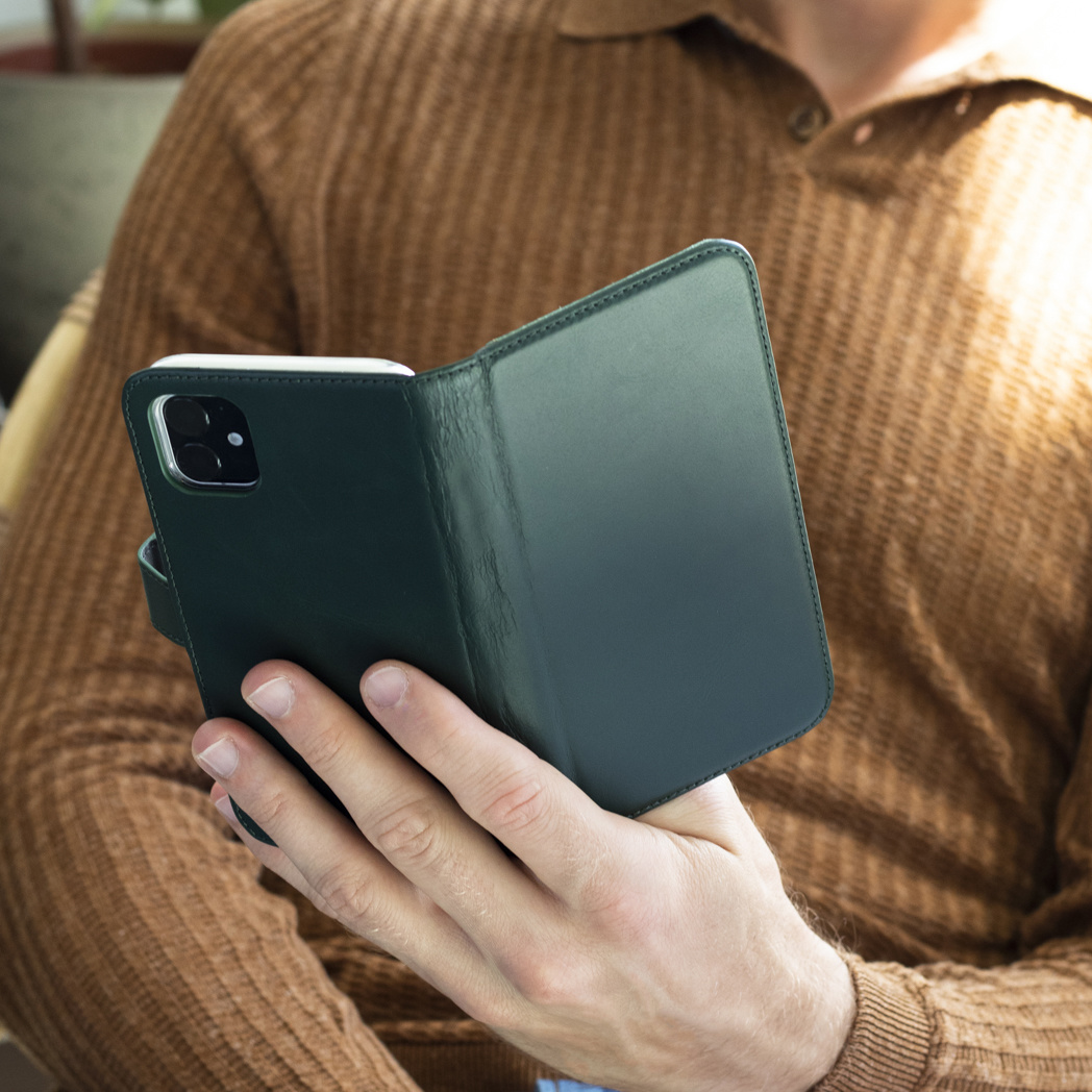 Een man in een bruine trui houdt een groene telefoonhoes open en toont een telefoon erin.