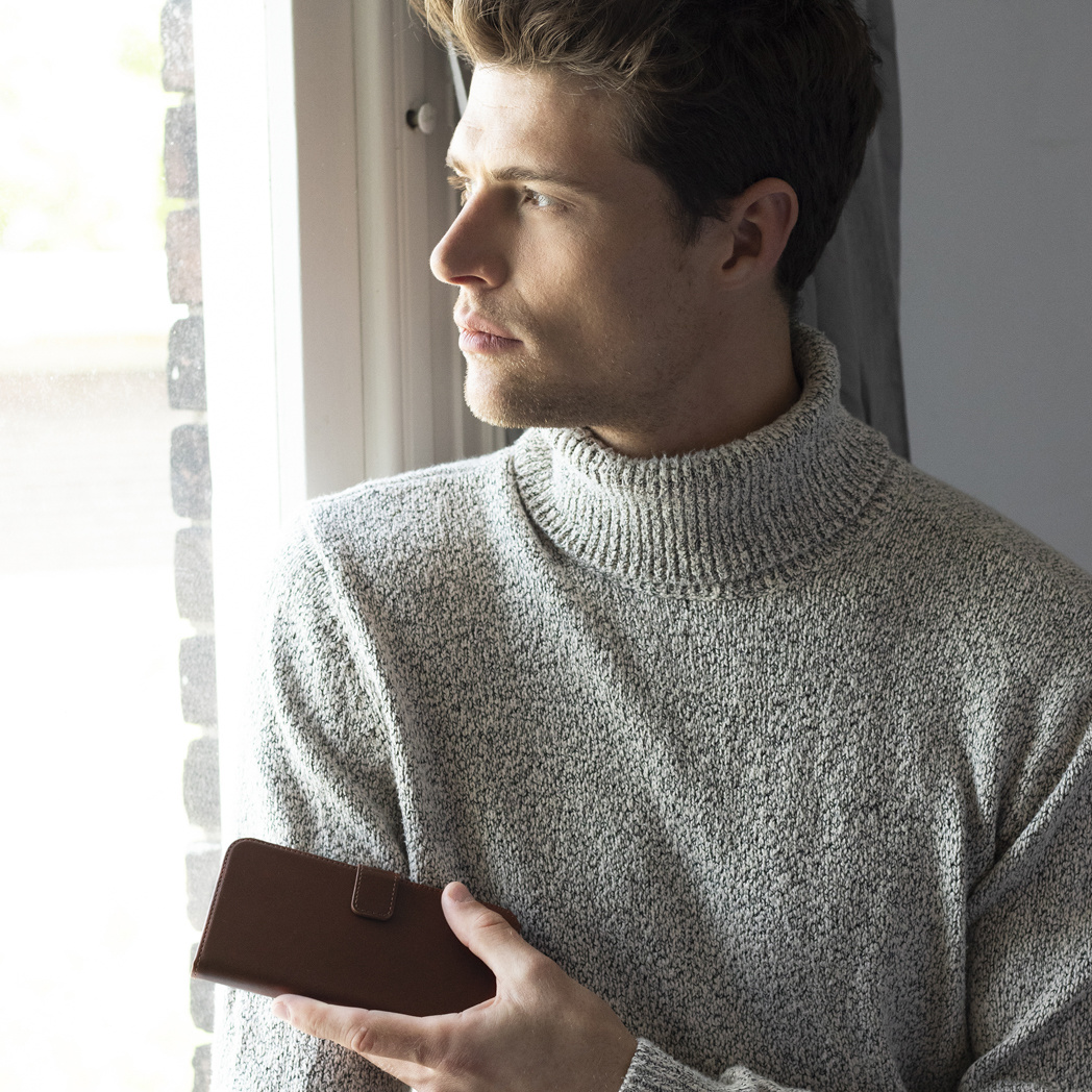 Homme regardant par une fenêtre tenant une coque de téléphone marron.