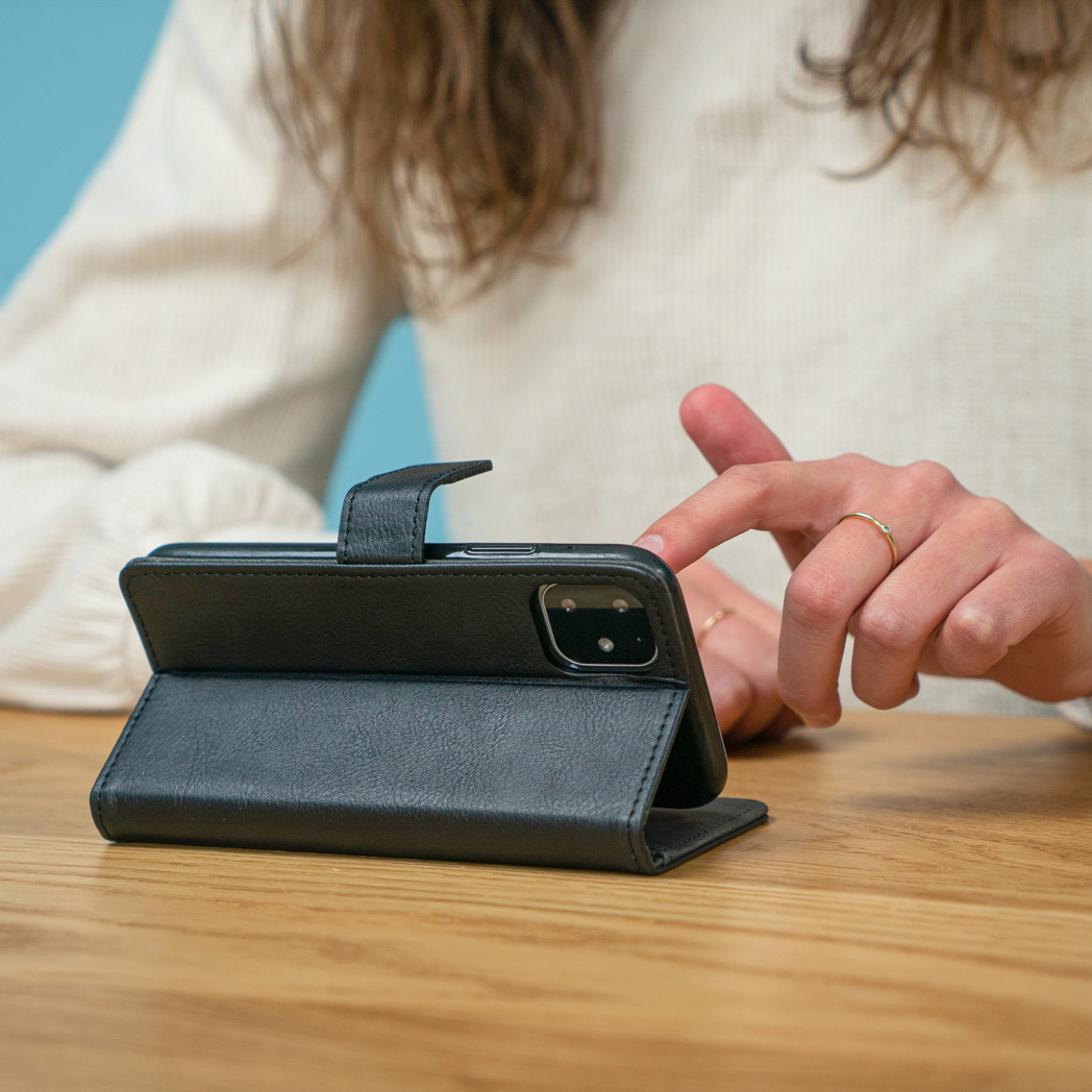 Una mano tocca un telefono su un tavolo. Il telefono è in una custodia a portafoglio nera aperta.