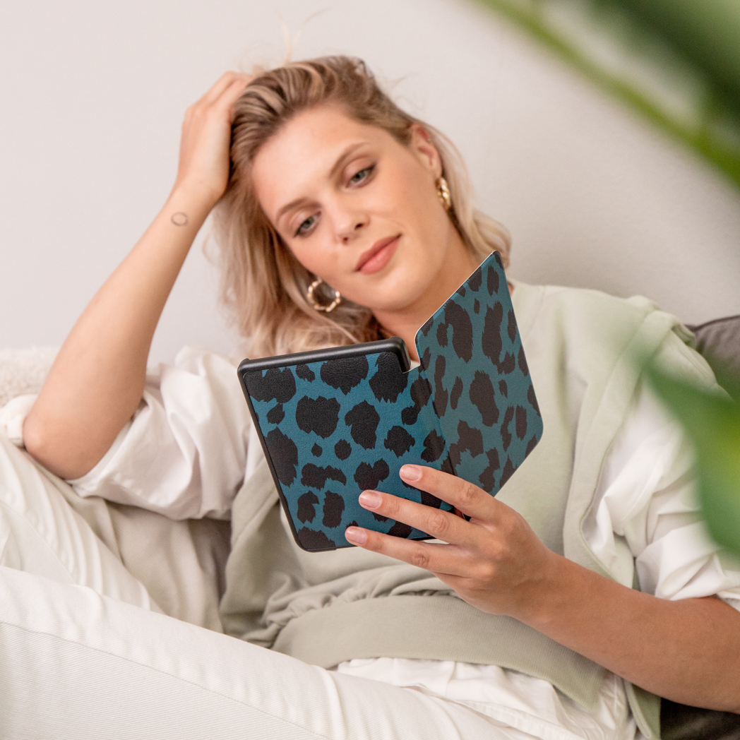 Femme tenant une liseuse dans un étui à imprimé léopard noir et bleu.