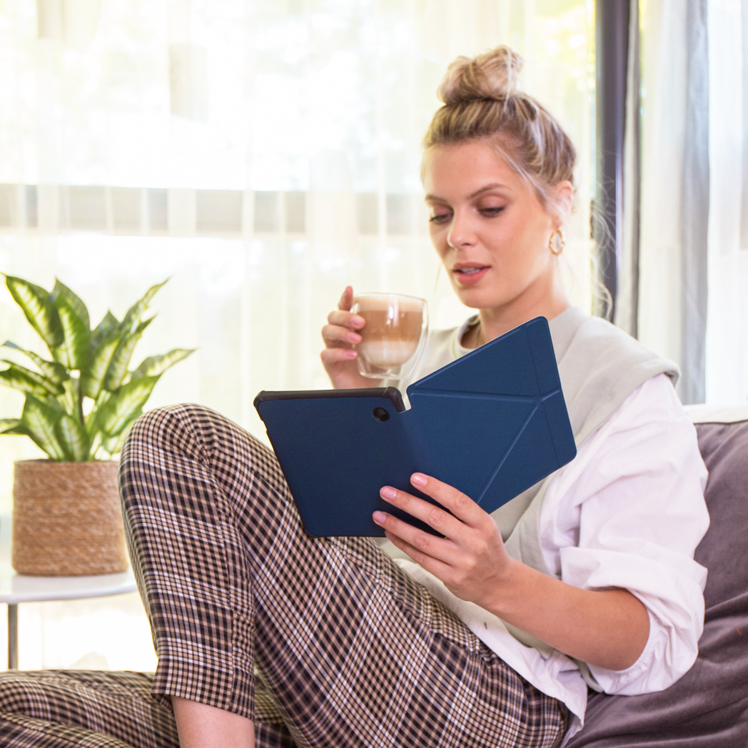 Vrouw houdt tablet en koffie vast, zit op een bank.