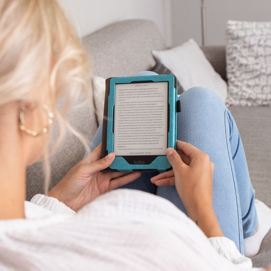 Vrouw in jeans houdt een Kobo e-reader vast, die tekst weergeeft. Ze zit op een bank met een kussen.