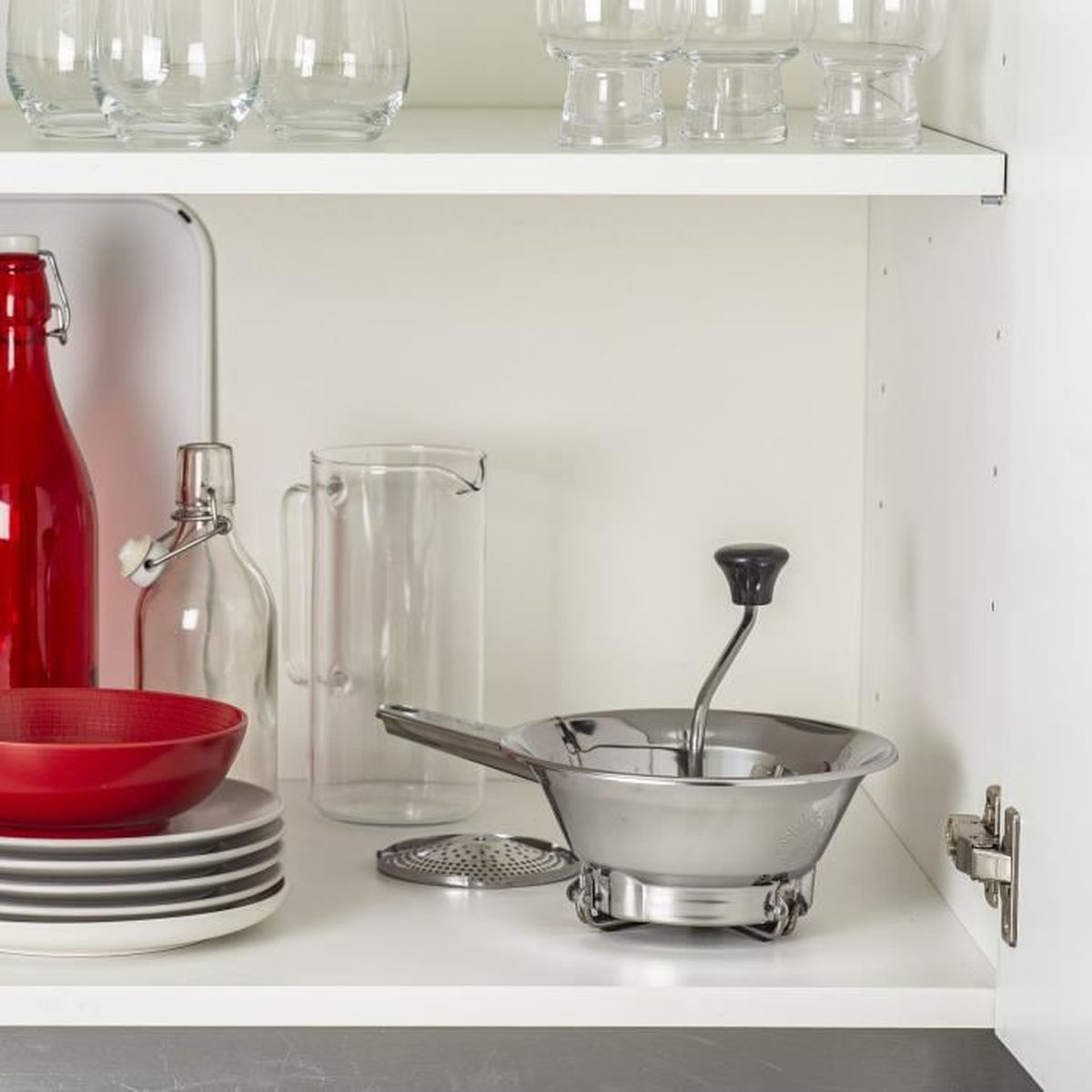Küchenschrank mit Flaschen, Schüssel, Tellern, Passiermühle. Weißer Schrank, graue Arbeitsplatte.