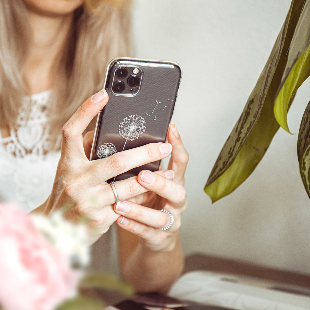 Vrouw houdt smartphone met paardenbloemontwerp op hoes, draagt ringen, close-up.