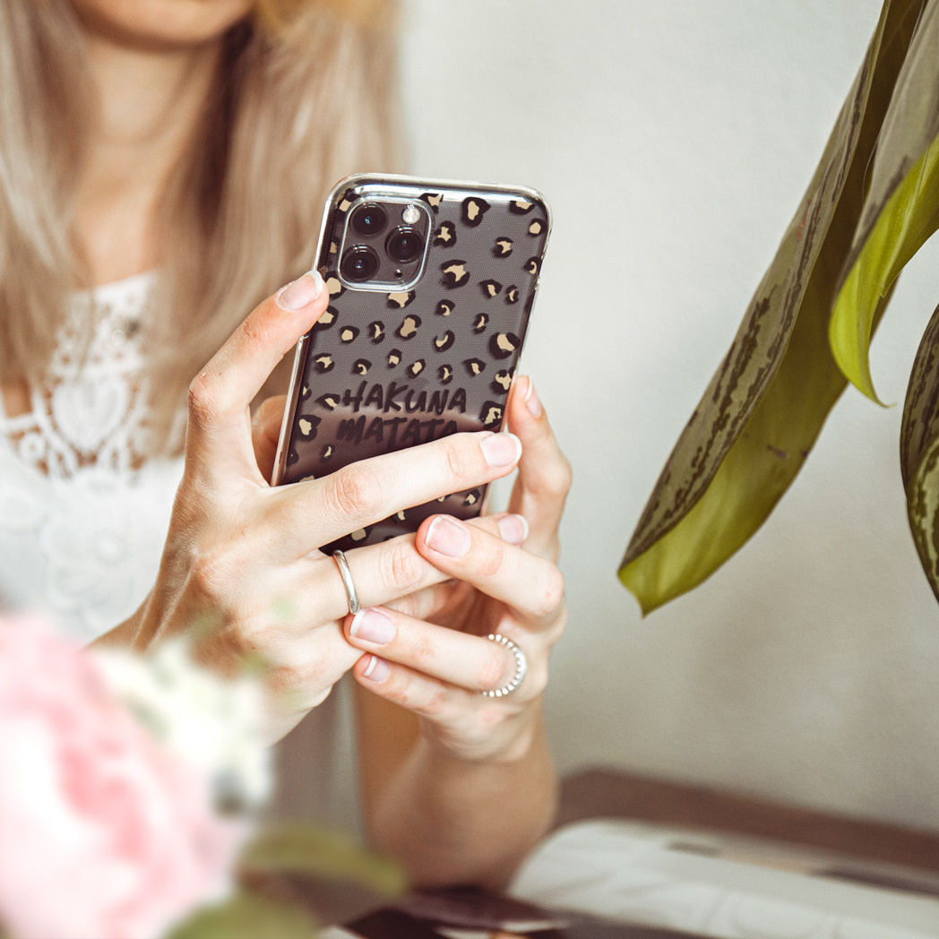 Femme tenant un téléphone avec une coque léopard. Le texte sur la coque dit Hakuna Matata.