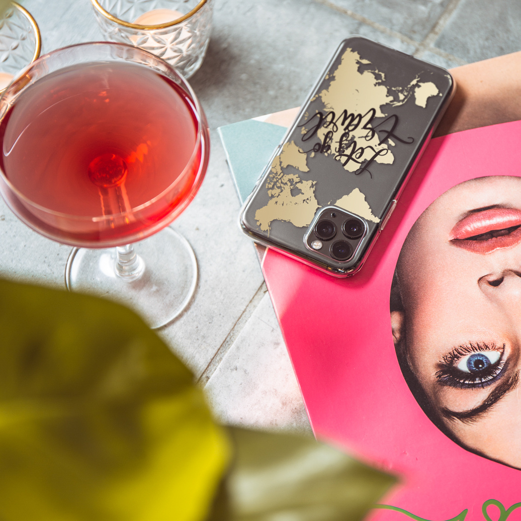 Telefoonhoesje met wereldkaart ontwerp, geplaatst met tijdschriften en een drankje.