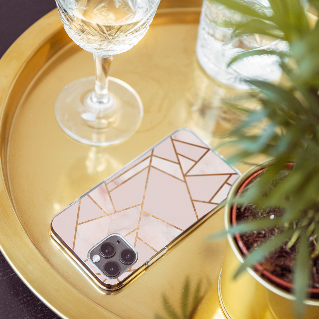 Telefoonhoesje met een roze marmerdesign met gouden accenten naast een cocktail en een plant.