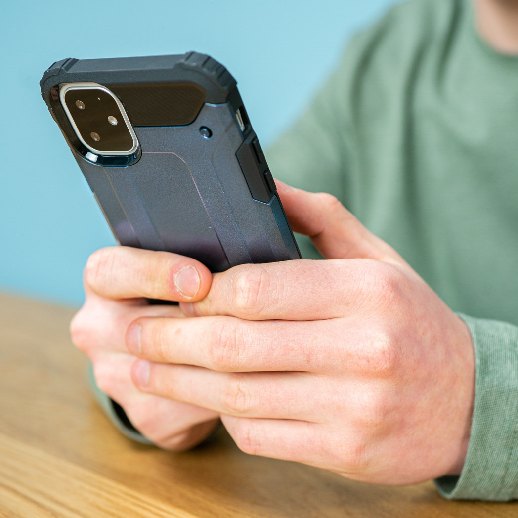 Personne tenant un téléphone avec étui bleu foncé sur une table en bois et fond bleu.