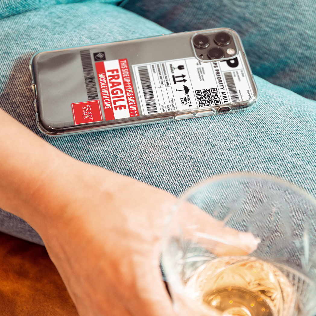 Een telefoon in een doorzichtig hoesje met een verzendlabel ligt op de schoot van een persoon in de buurt van een glas wijn.