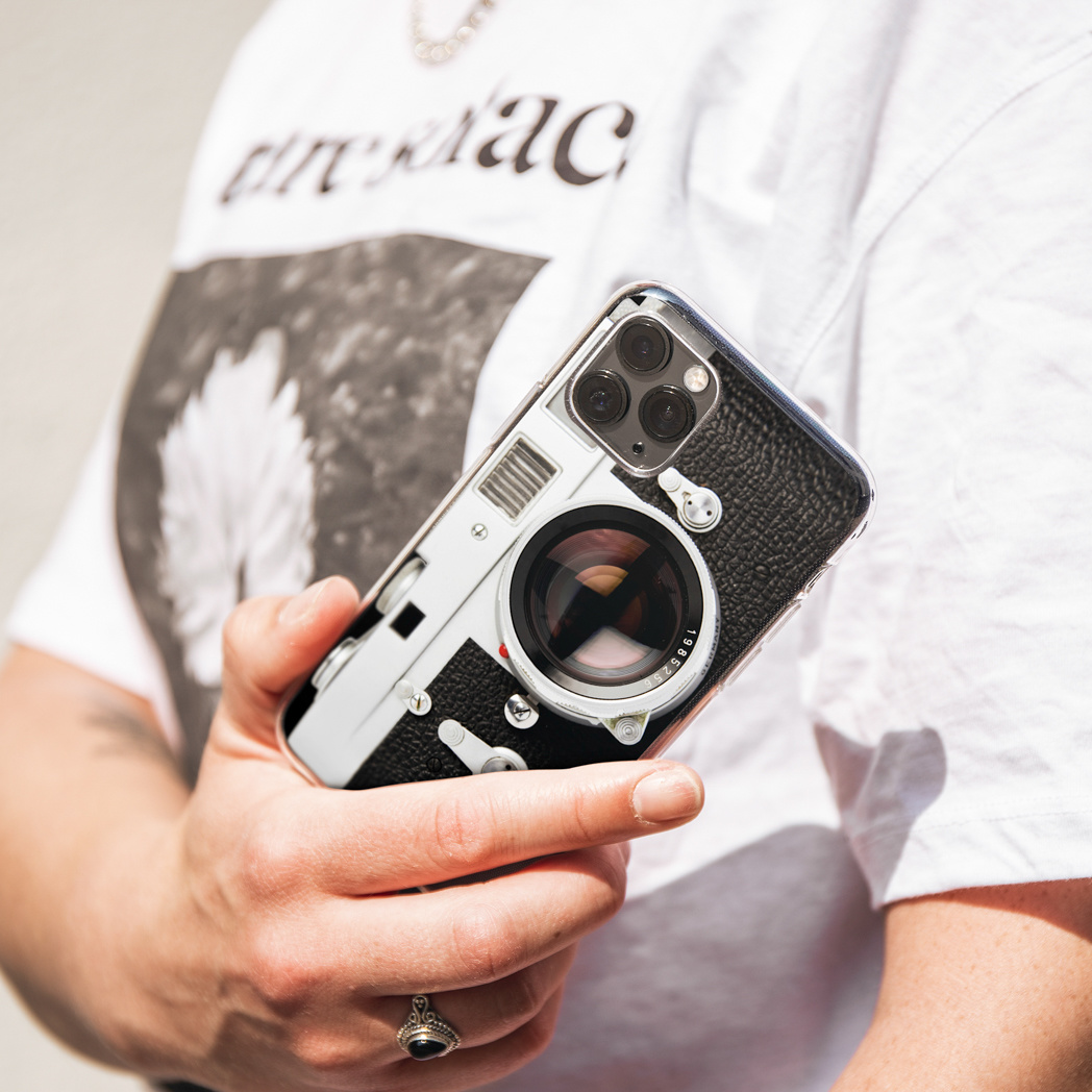 Persoon houdt een telefoonhoesje met een camera-ontwerp vast. De achtergrond is wit.