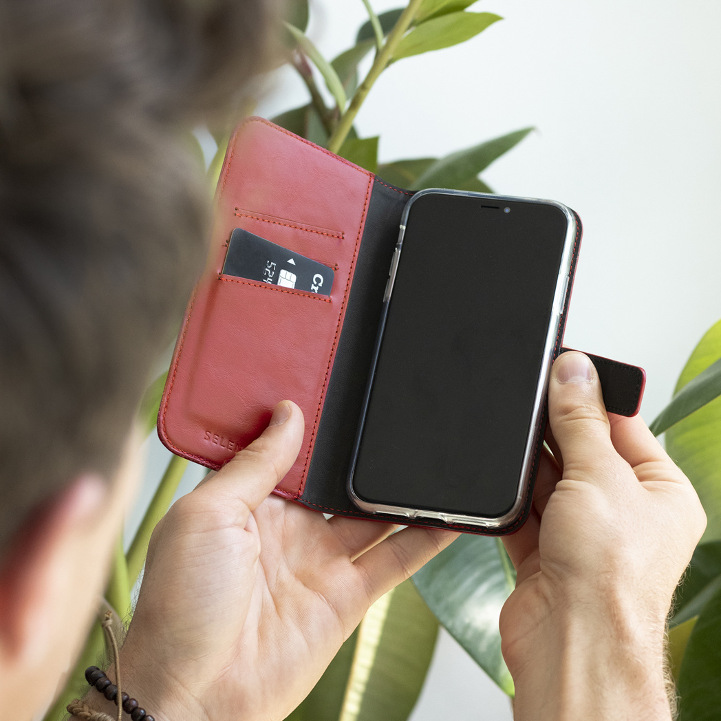 Una persona che tiene un telefono in una custodia di pelle rossa, vicino a piante verdi.