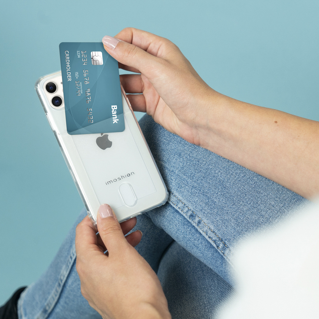 Des mains tiennent un téléphone avec une carte de crédit. Fond bleu. Le téléphone est dans une coque transparente.