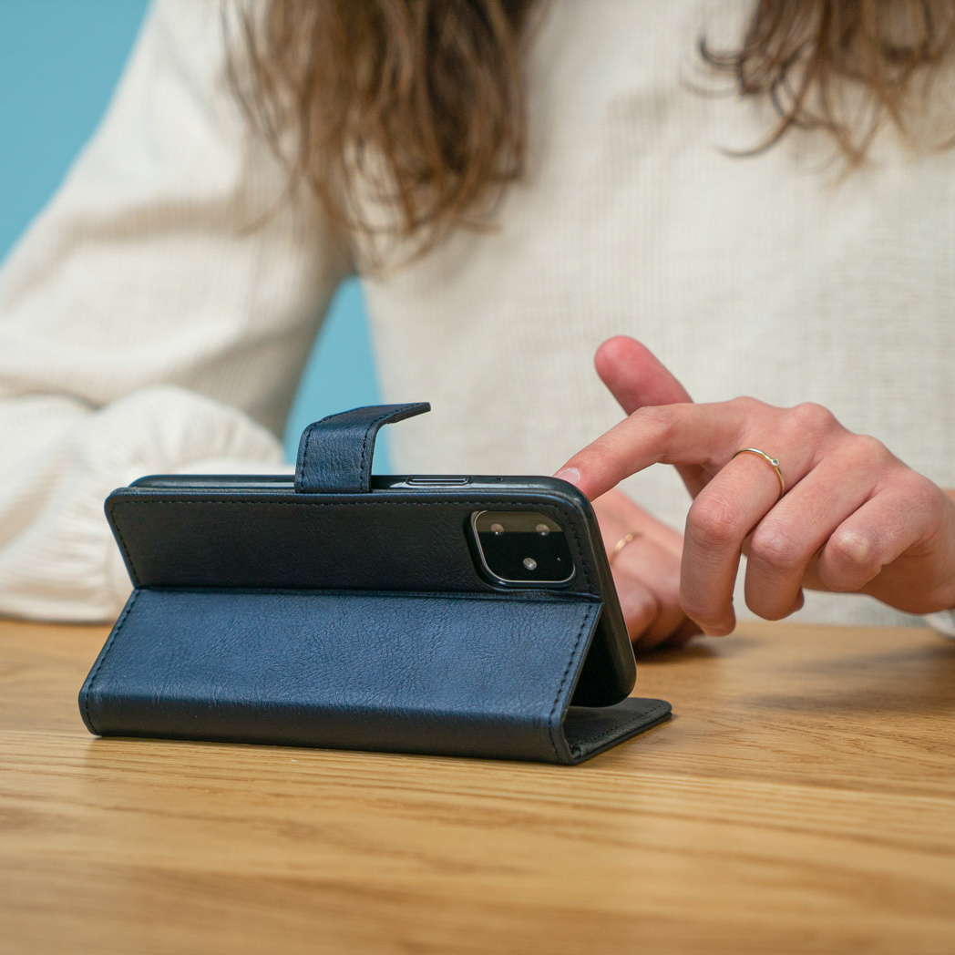 La mano di una persona usa una custodia per telefono su un tavolo di legno, mostrando il telefono all'interno.