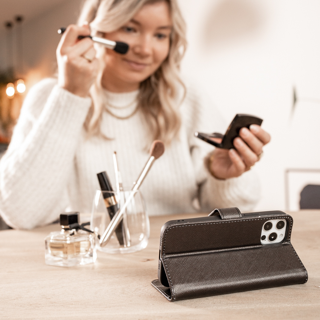 Femme utilisant un pinceau de maquillage avec un étui de téléphone ouvert devant elle sur une table.