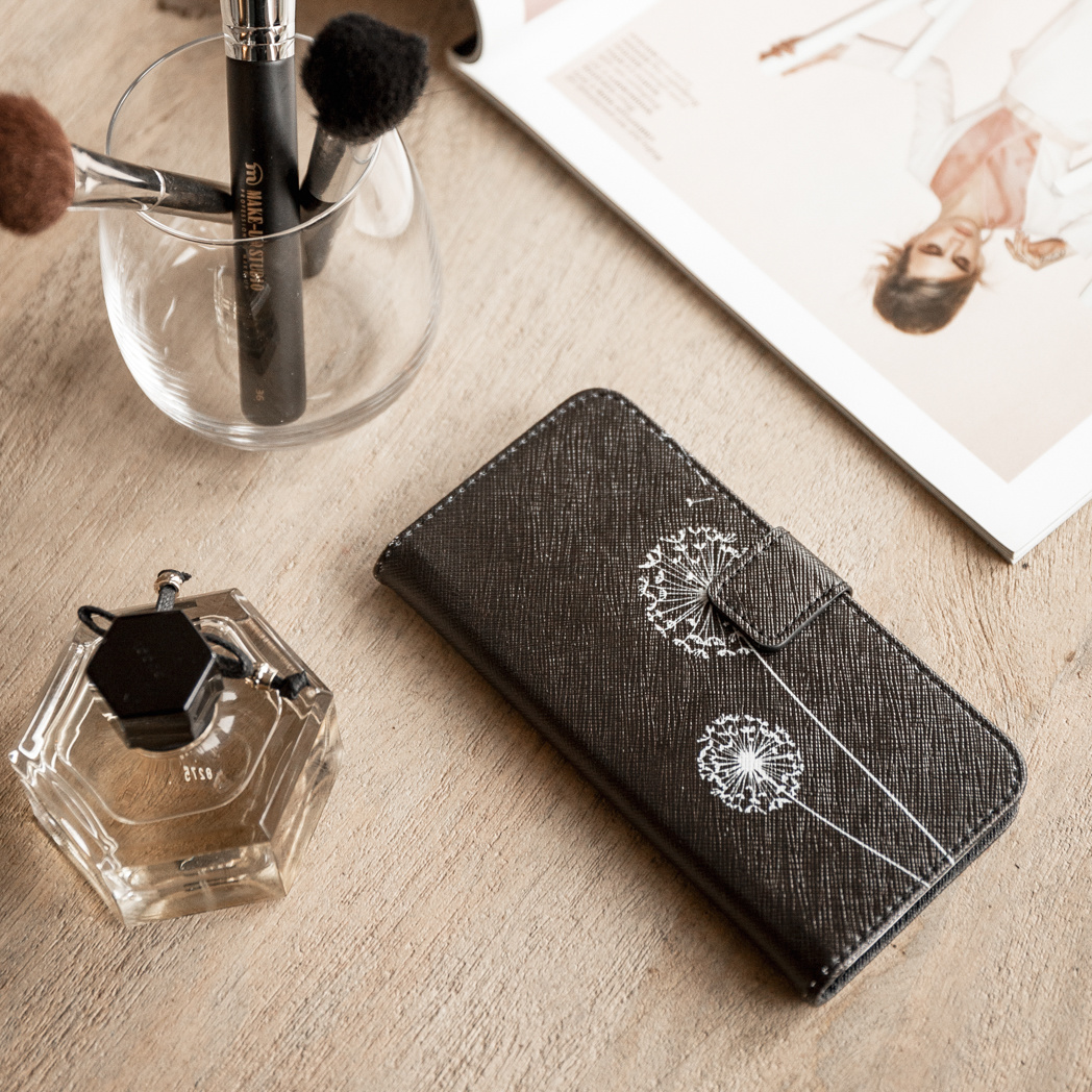 Étui de téléphone avec motif de pissenlit, parfum, pinceaux et un magazine sur bois.