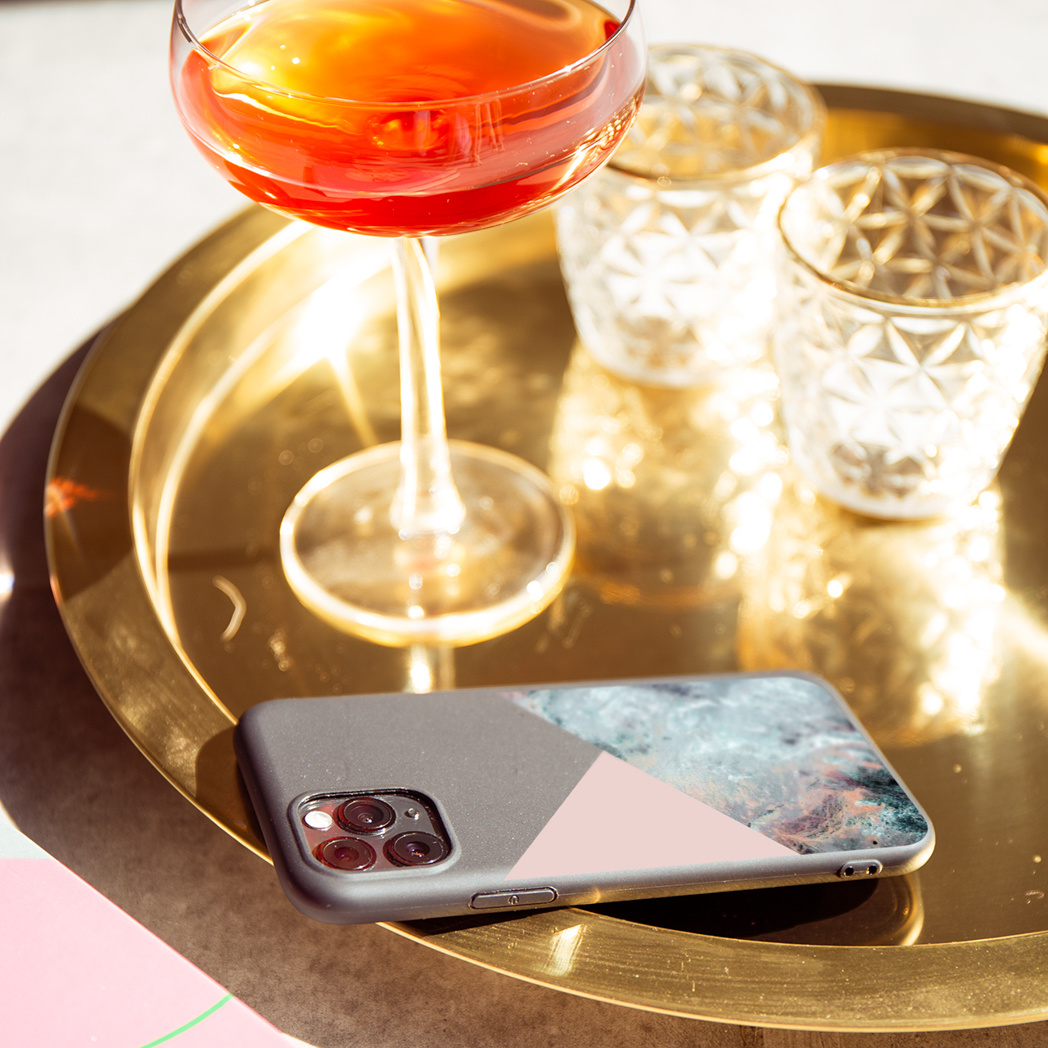 Een gouden dienblad met een cocktail, twee kandelaars en een telefoonhoesje met een kleurrijk design.