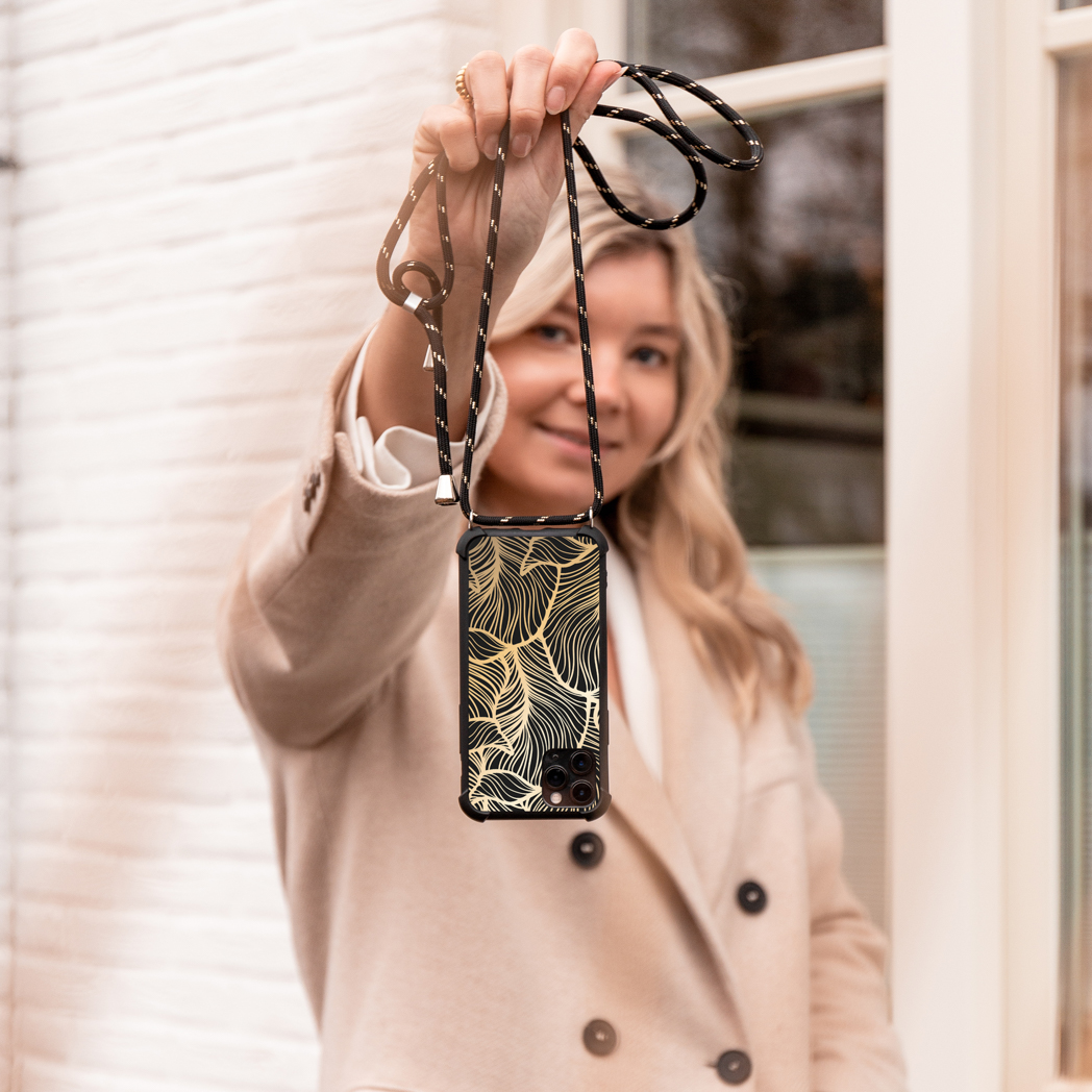 Blonde vrouw houdt een zwart telefoonhoesje met een riem vast, met gouden bladeren.