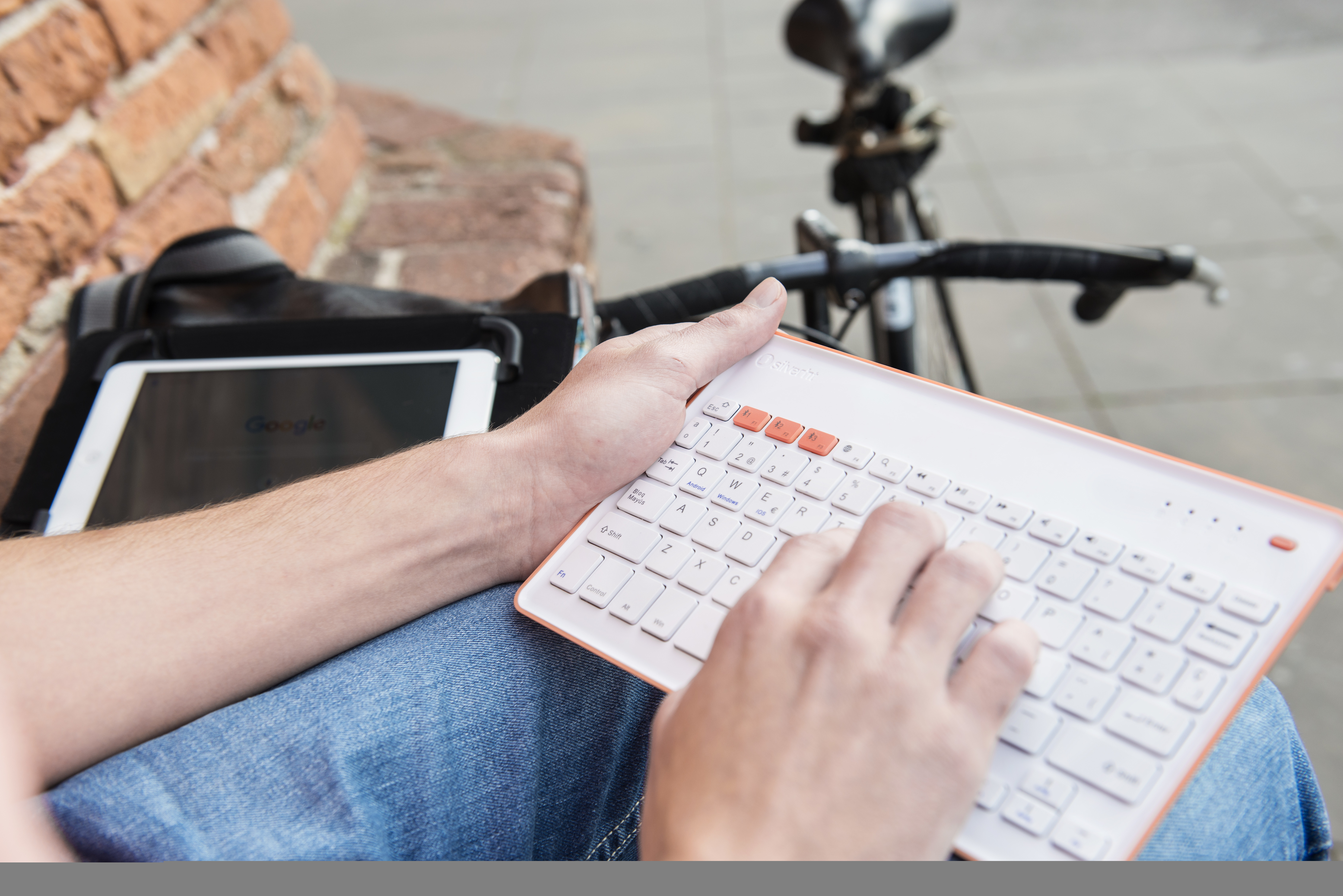 Persona che usa una tastiera bianca e arancione accanto a un tablet.