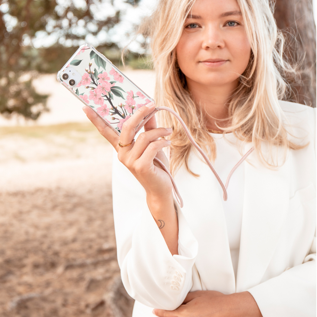 Blonde vrouw die een telefoon met een bloemenhoes vasthoudt. De telefoon is verbonden met een bandje.