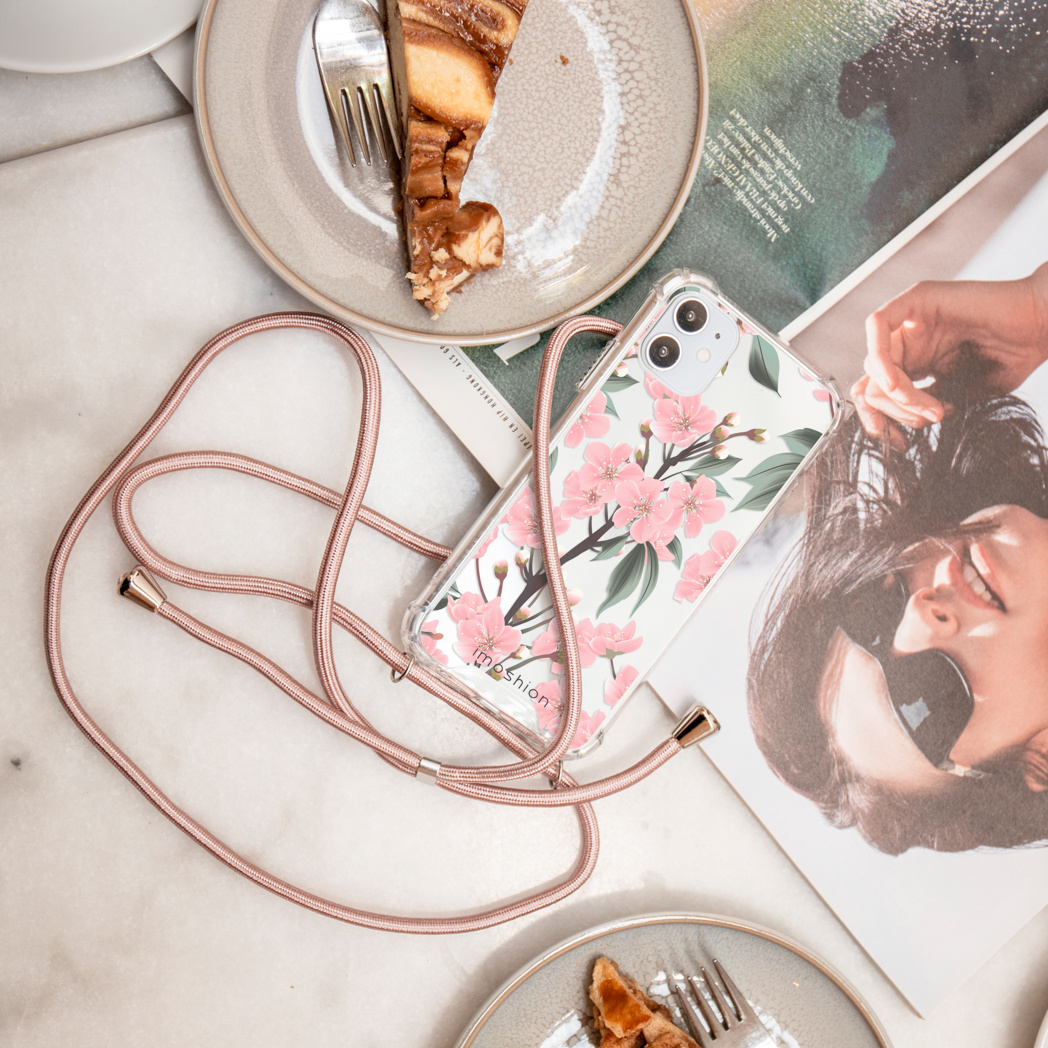 Telefoonhoes met roze bloemenontwerp, bevestigd aan een koord, op een tafel.