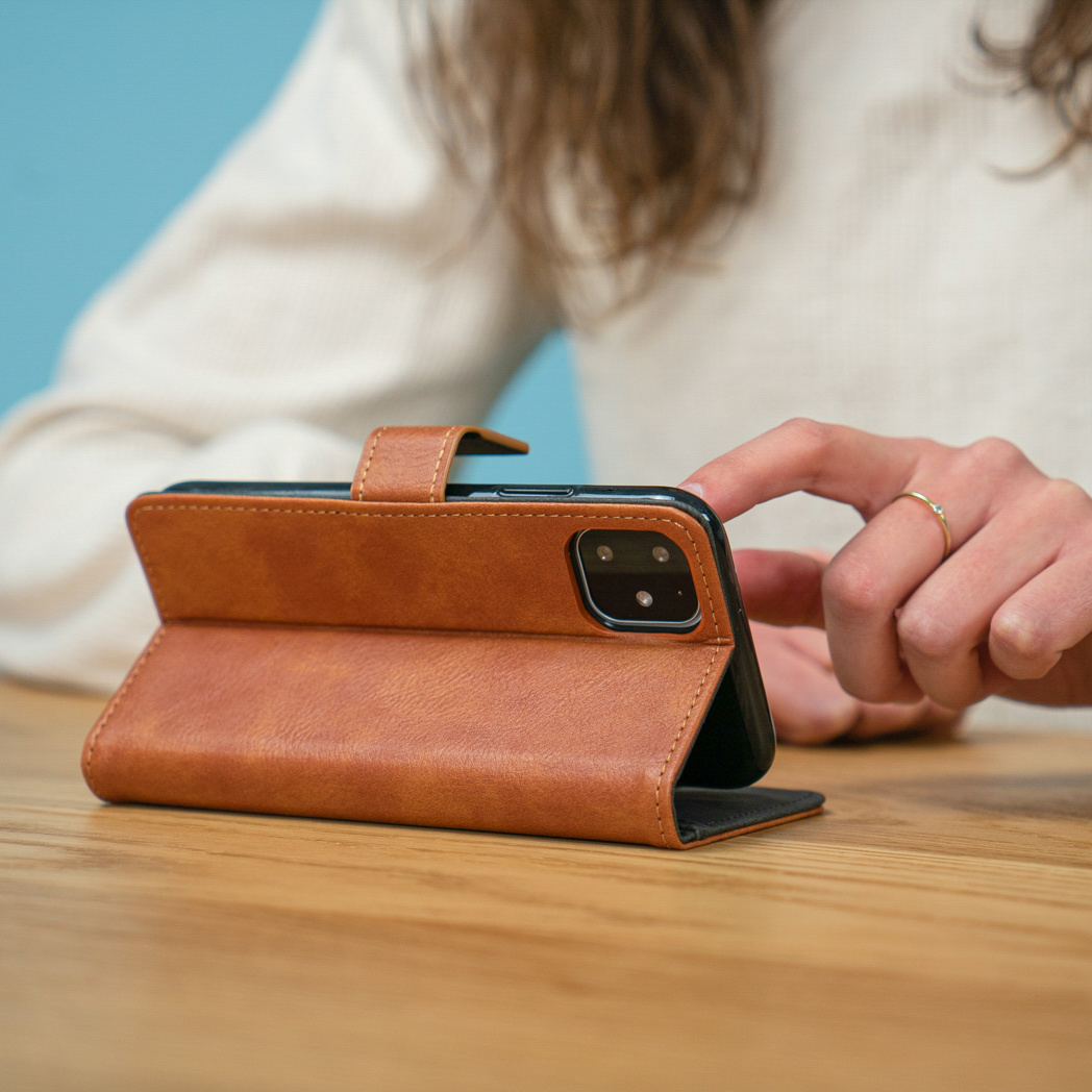 Bruine telefoonhoes in gebruik op een houten tafel. Een persoon raakt het scherm aan.