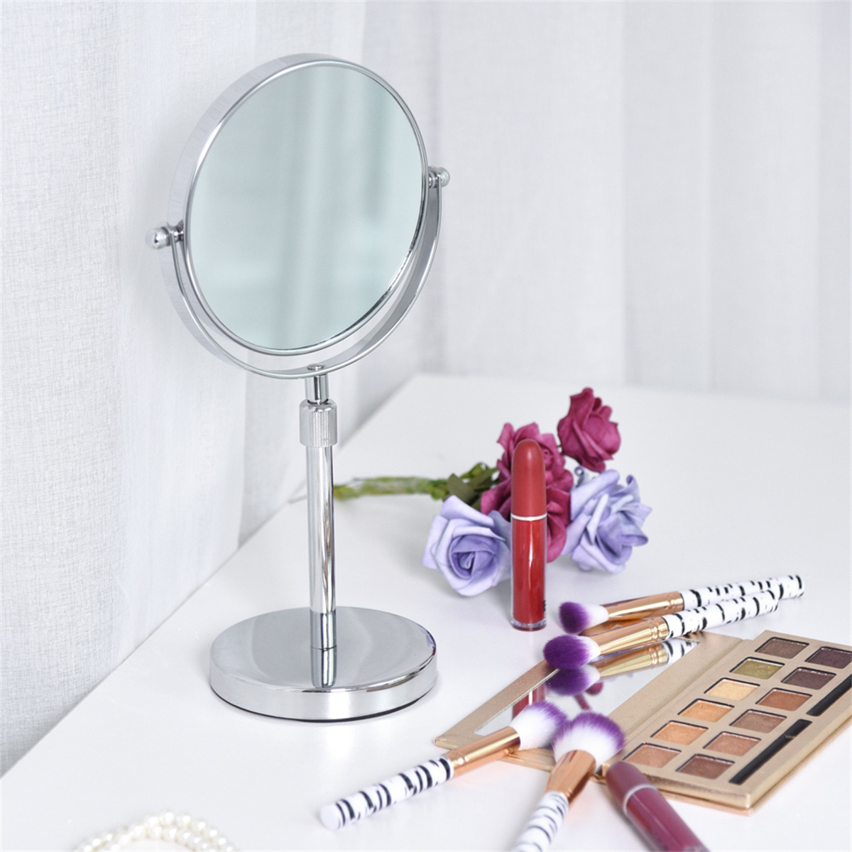 Make-up-Utensilien auf einem weißen Tisch: Spiegel, Pinsel, Lippenstift und Rosen.