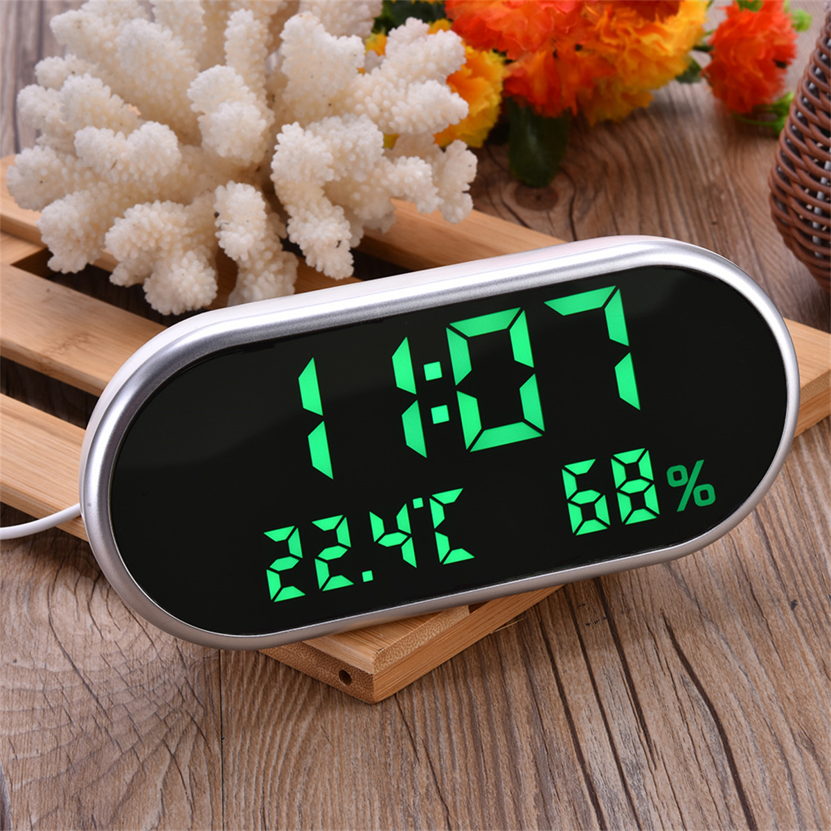 Digitaluhr mit Zeit, Datum und Luftfeuchtigkeit. Silberner Rahmen, schwarzer Bildschirm und Holzgrund.