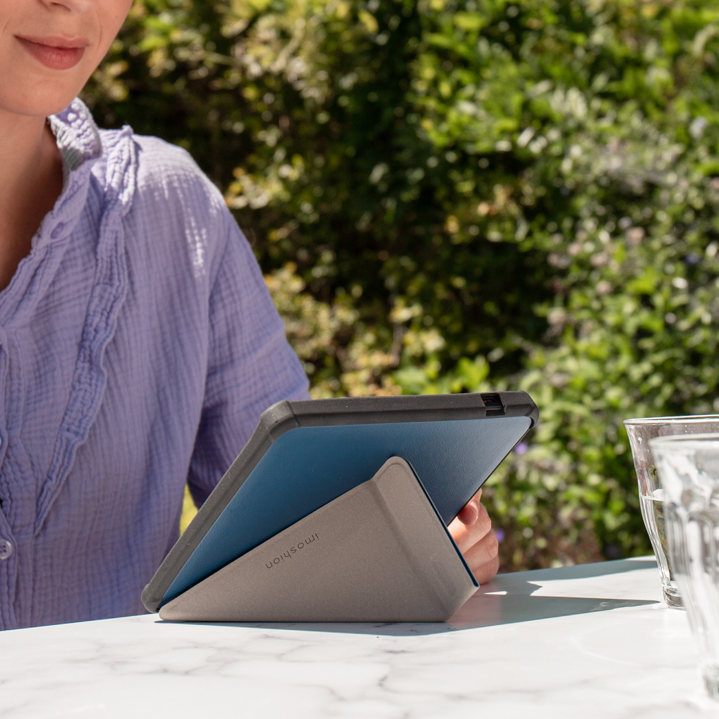 Une personne tient une tablette dans un étui. Ils sont dehors avec du feuillage vert et un verre d'eau.