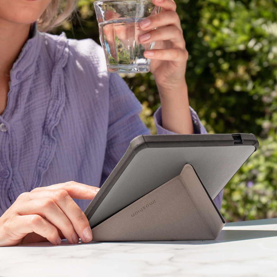 Een vrouw houdt een glas water vast terwijl ze een tablet op een standaard buiten gebruikt.