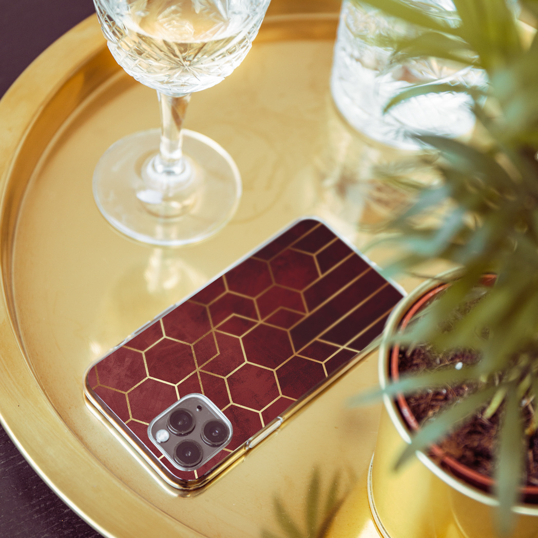 Telefoonhoesje met goudkleurig zeshoekig ontwerp, op een gouden dienblad naast een plant en een glas.